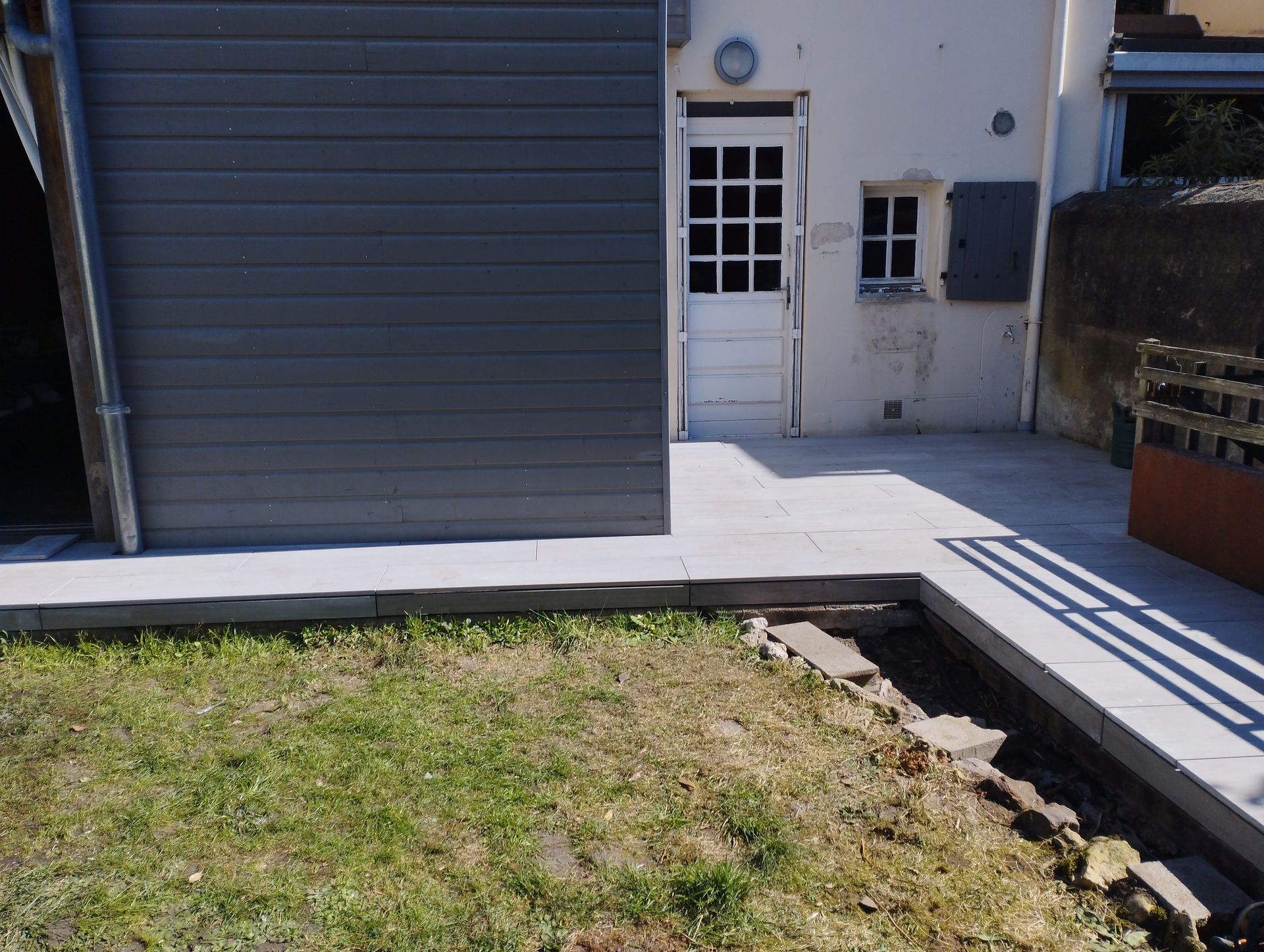 Terrasse en béton gris avec porte blanche, donnant sur un jardin gazonné.