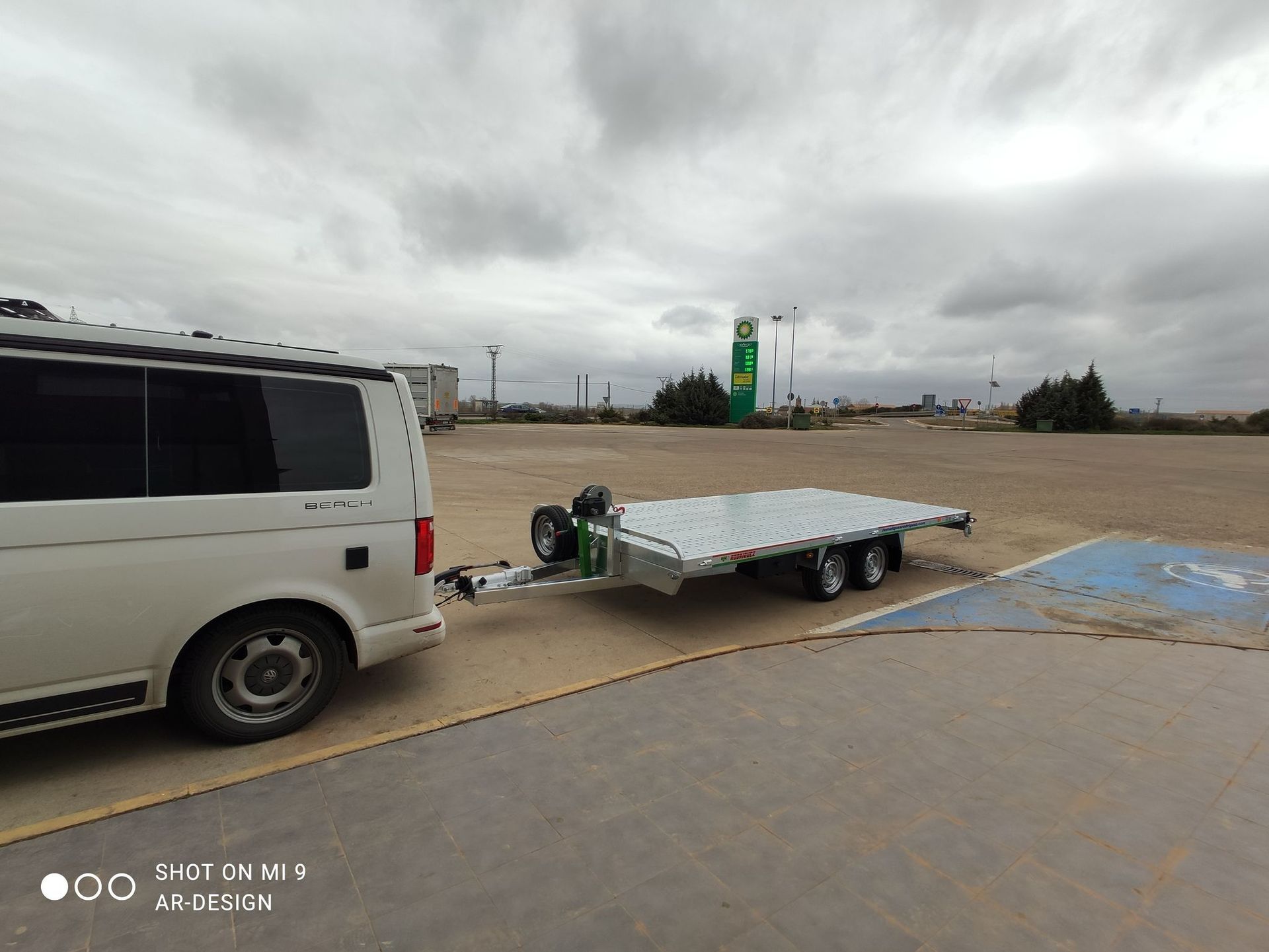 Una camioneta blanca remolcando un remolque plateado en un estacionamiento bajo un cielo nublado.