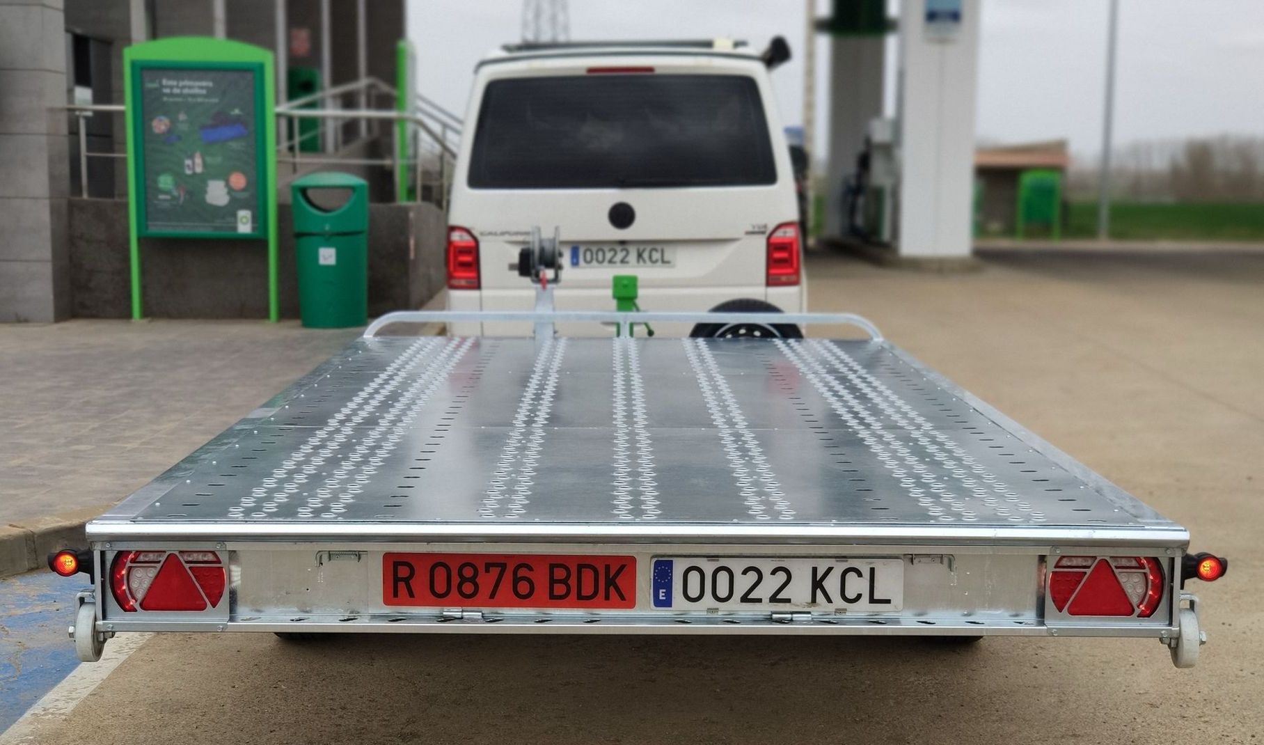 Un remolque transportador de automóviles de color blanco con matrícula y una camioneta blanca estacionada