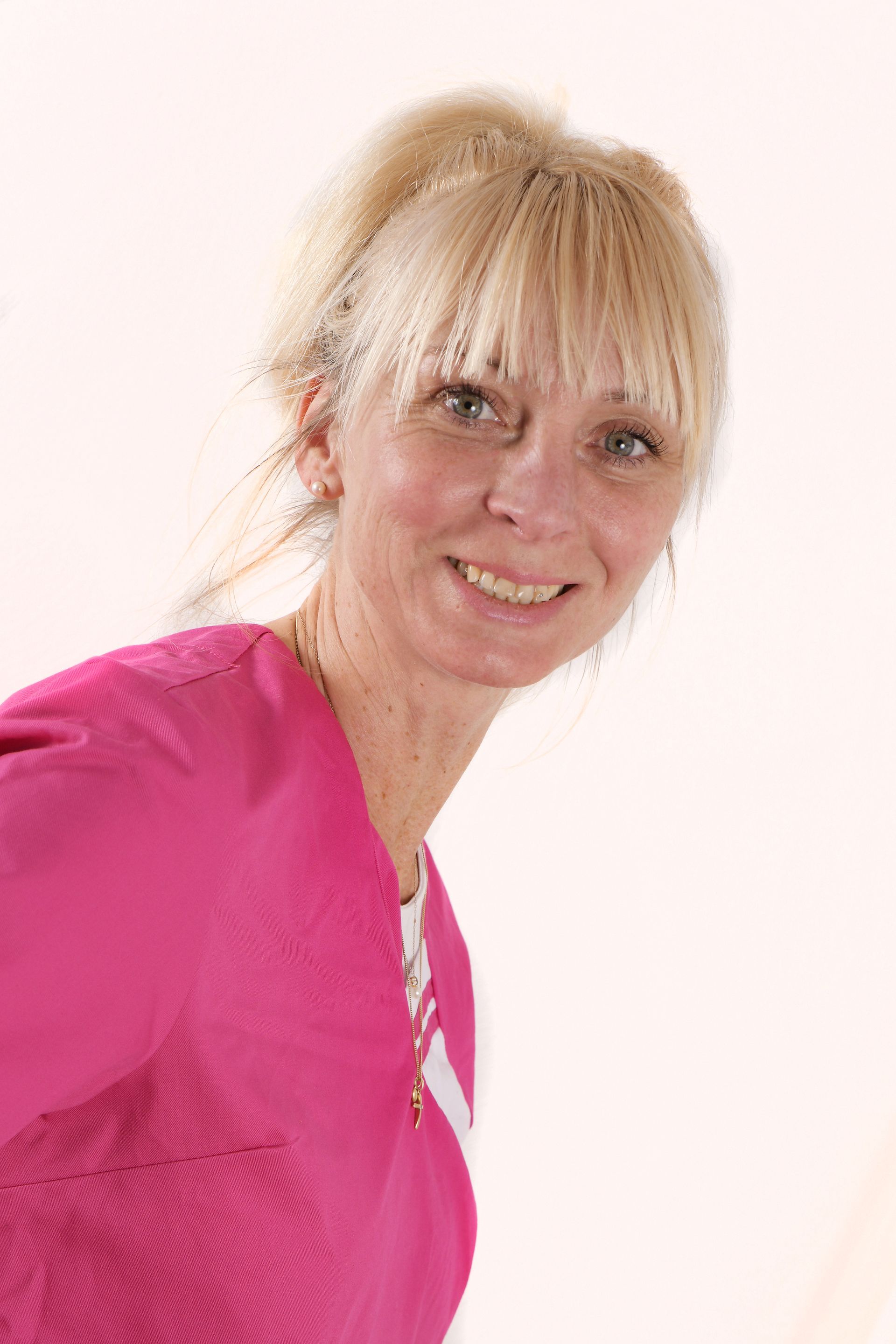 Porträtaufnahme einer freundlich lächelnden, blonden Frau vor hellem Hintergrund.