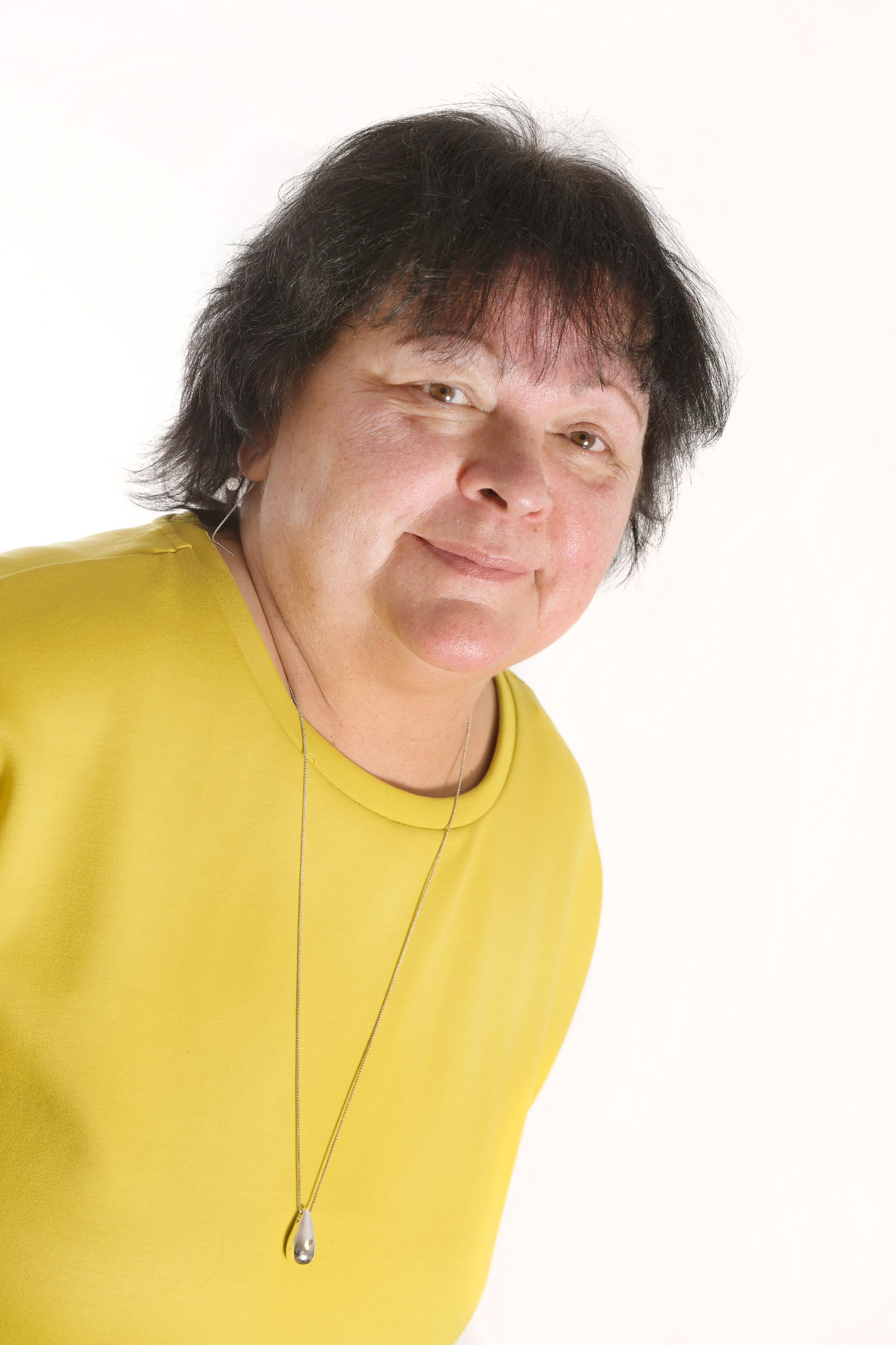 Portrait von Frau Georgy, der Verwaltungsleitung, mit kurzen, dunklen, lockigen Haaren und einem leichten Schmunzeln.