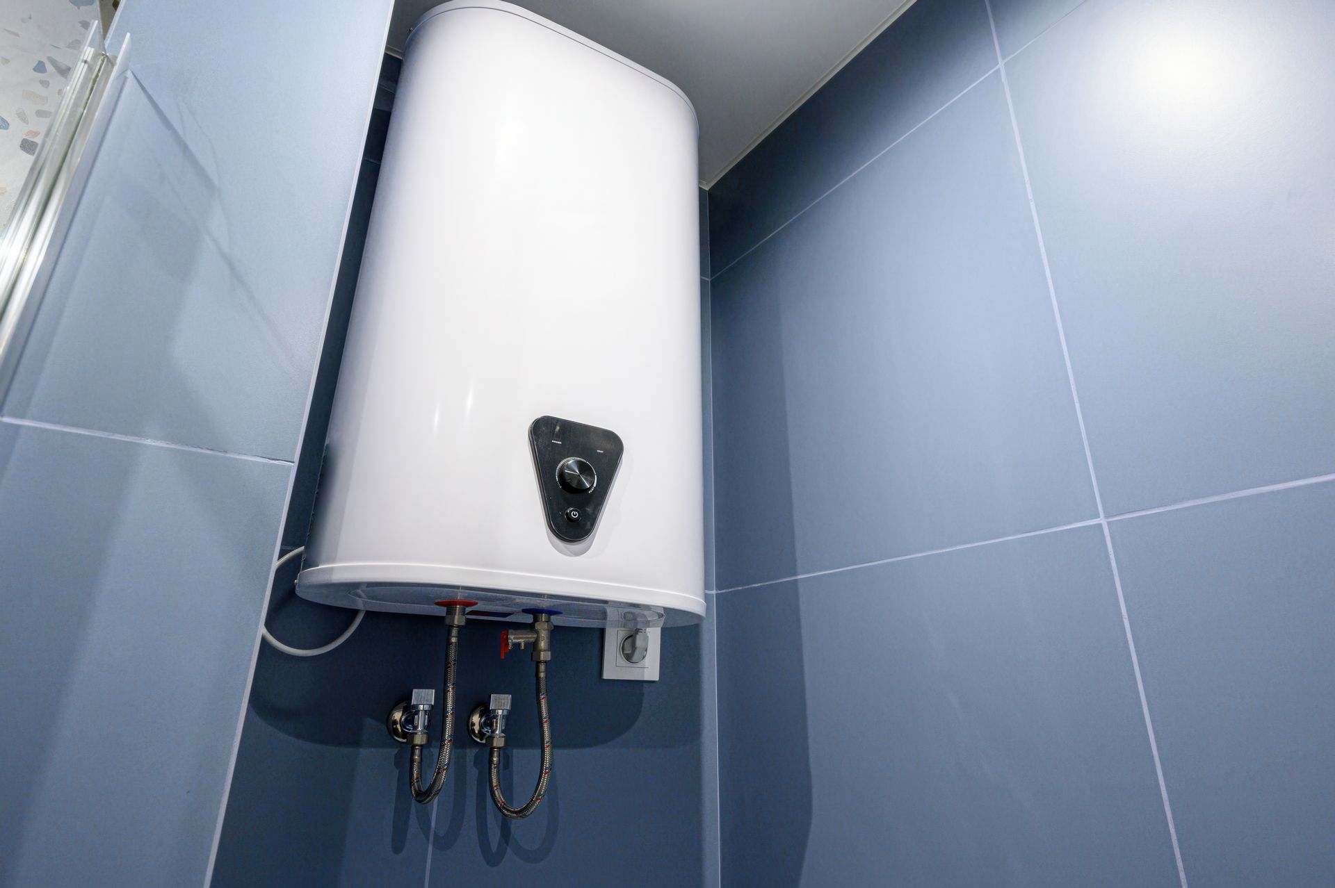 Un chauffe-eau blanc fixé en hauteur sur un mur carrelé de bleu.
