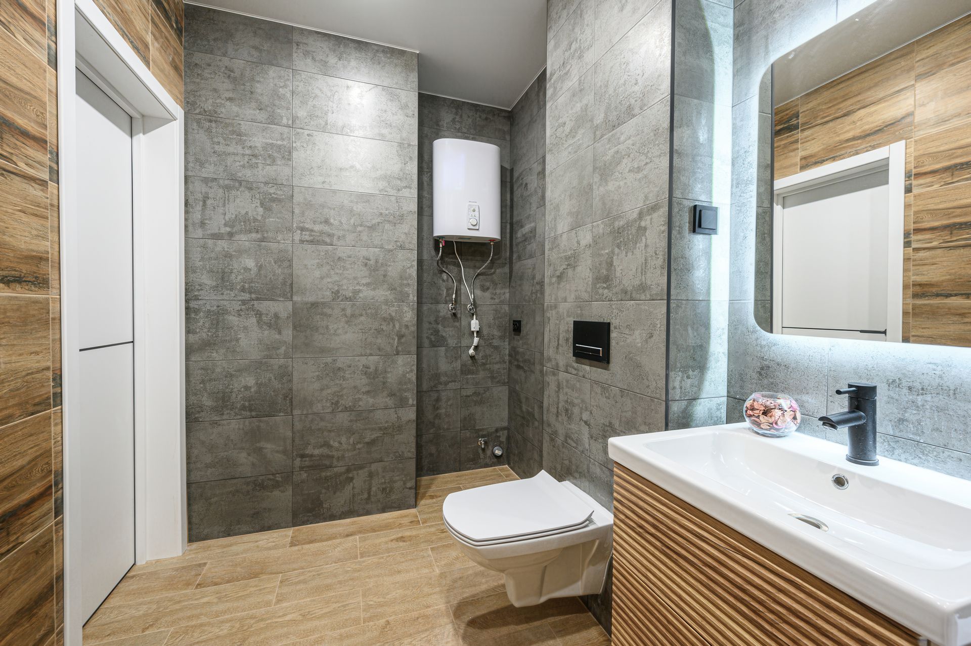 Une salle de bains moderne avec des murs carrelés gris, un meuble lavabo en bois et des toilettes suspendues.