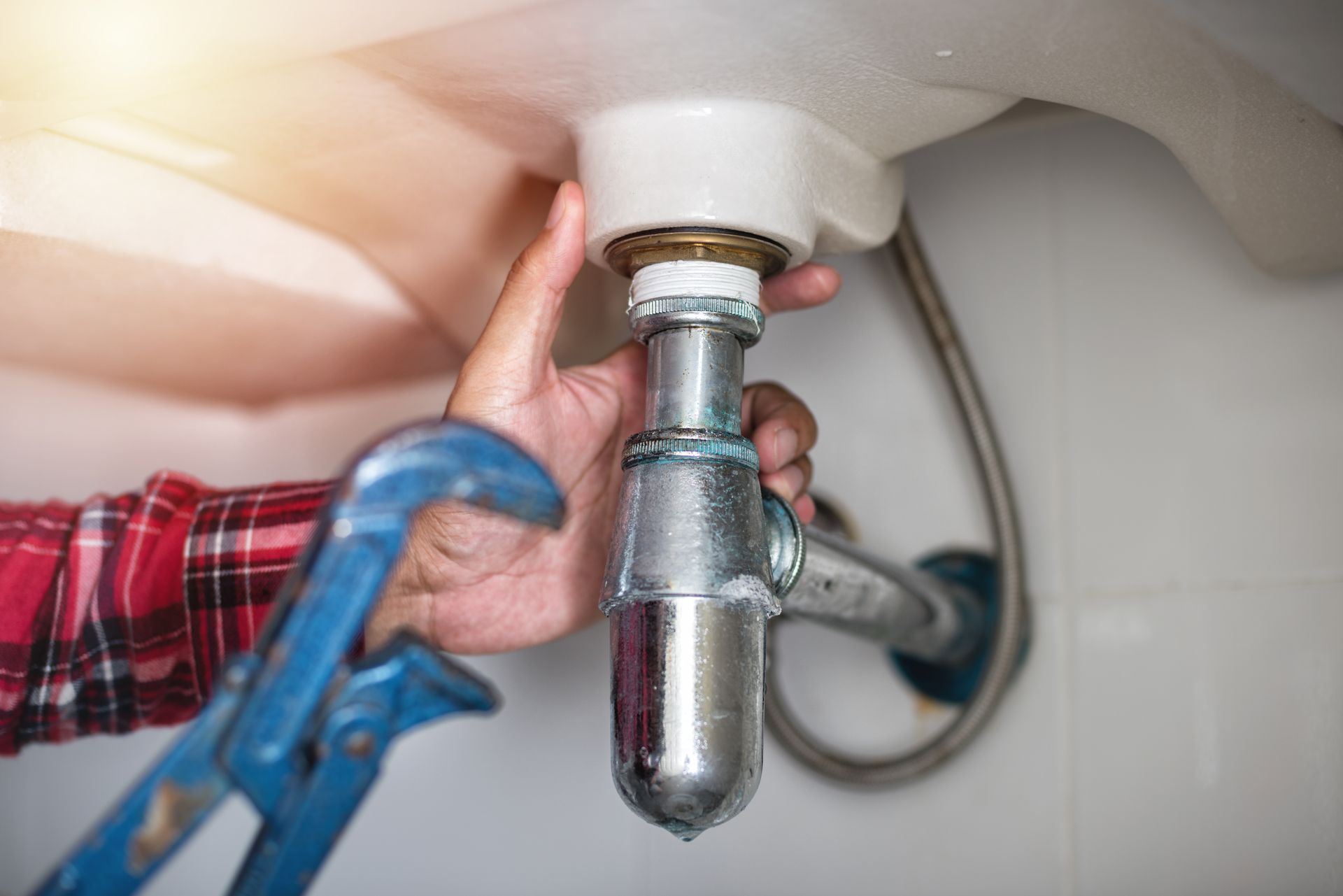 Un plombier resserre un tuyau d'évacuation d'évier sous un lavabo à l'aide d'une clé.