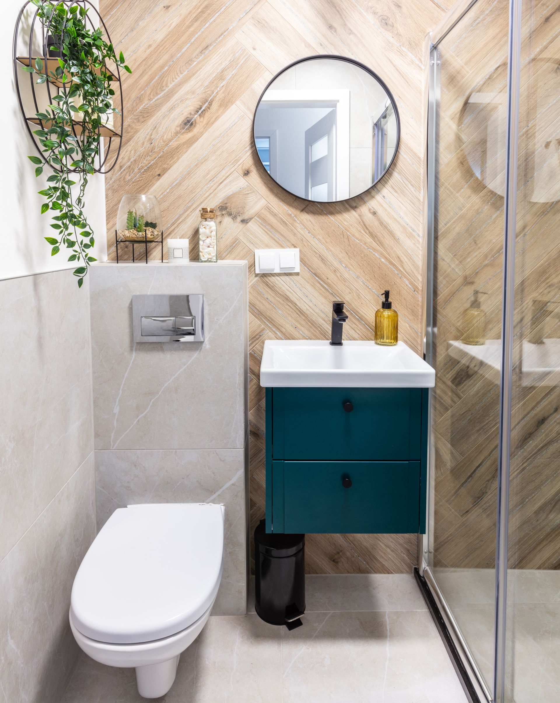 Une salle de bains moderne avec toilettes, meuble lavabo, miroir rond, douche et plante en pot.