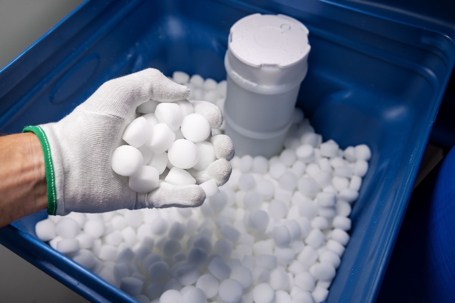 Une main remplit un adoucisseur d'eau de pastilles de sel.
