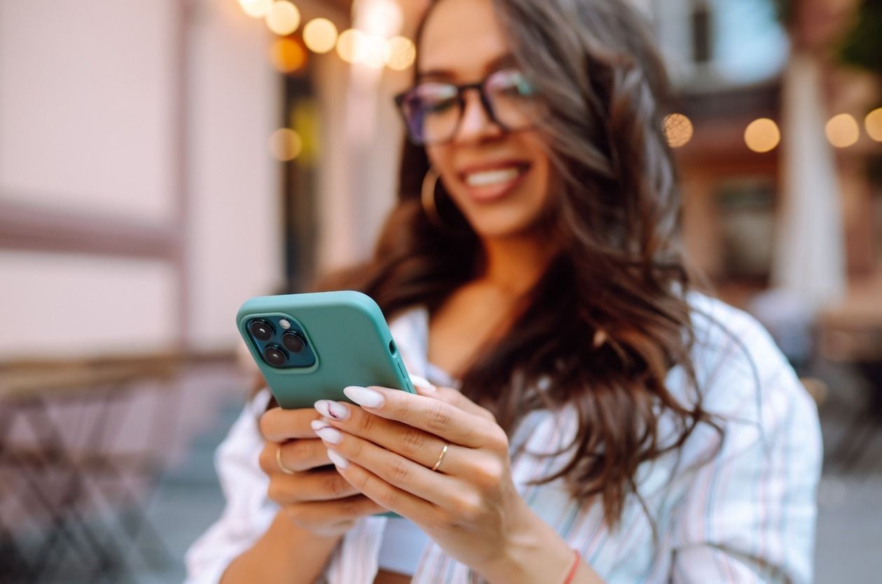 Una mujer que lleva gafas sostiene un teléfono móvil en sus manos.