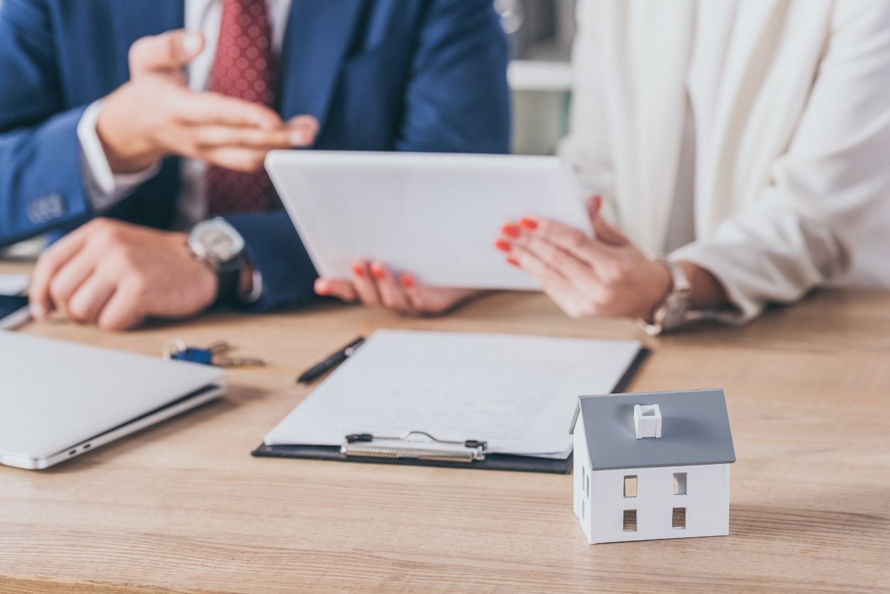 Agentes inmobiliarios revisando documentos con una pequeña maqueta de casa en un escritorio.