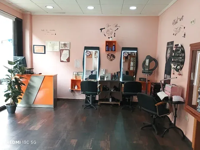 Interior de una peluquería con paredes rosas, suelo de madera oscura, espejos, sillas y utensilios de peluquería.