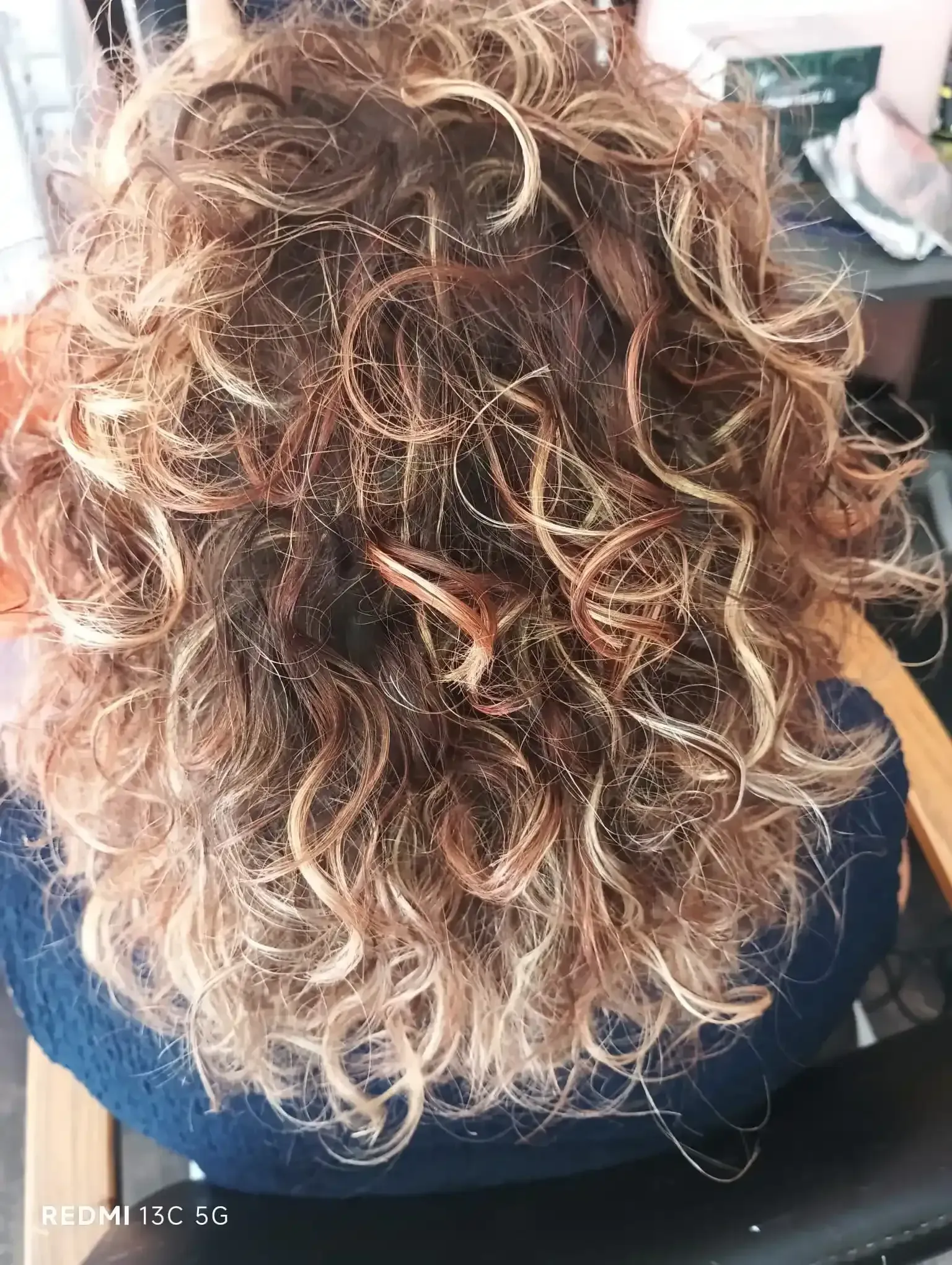 Cabello rizado castaño y rubio con reflejos, peinado con rizos sueltos.