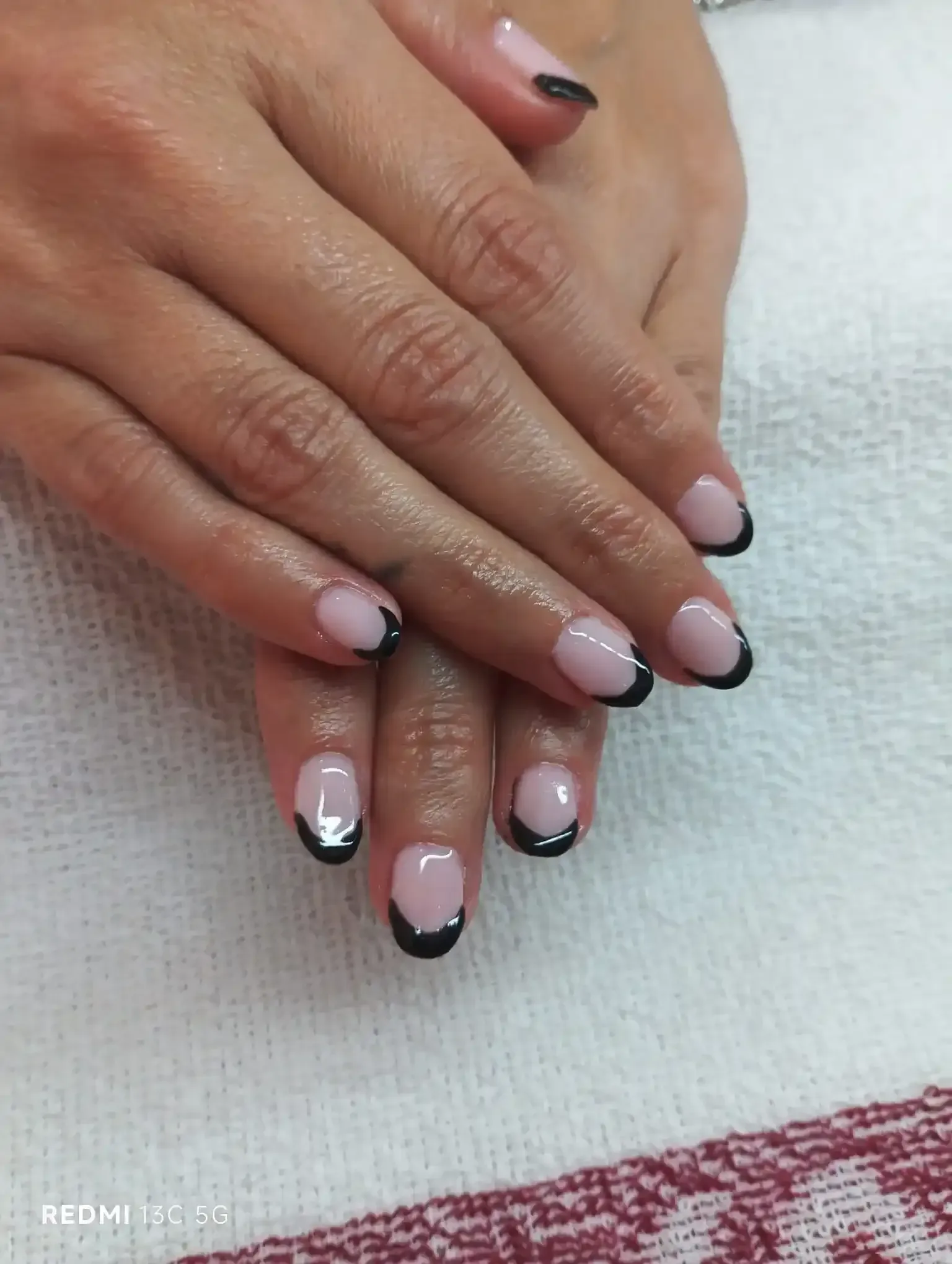 Manos con manicura francesa, puntas negras sobre una base de uñas blanca y transparente.