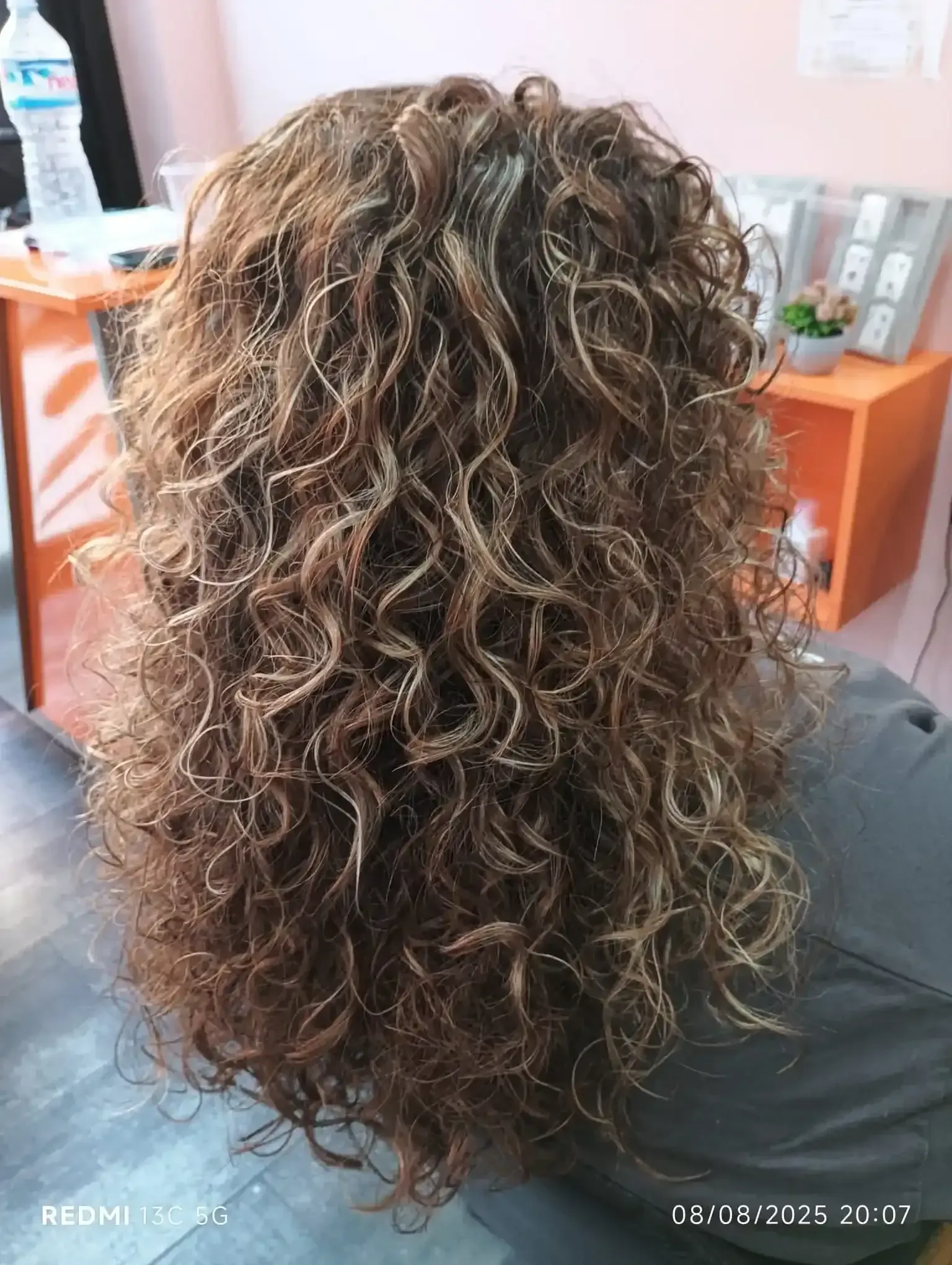 Cabello castaño rizado con reflejos rubios. En interiores, en un salón de belleza.