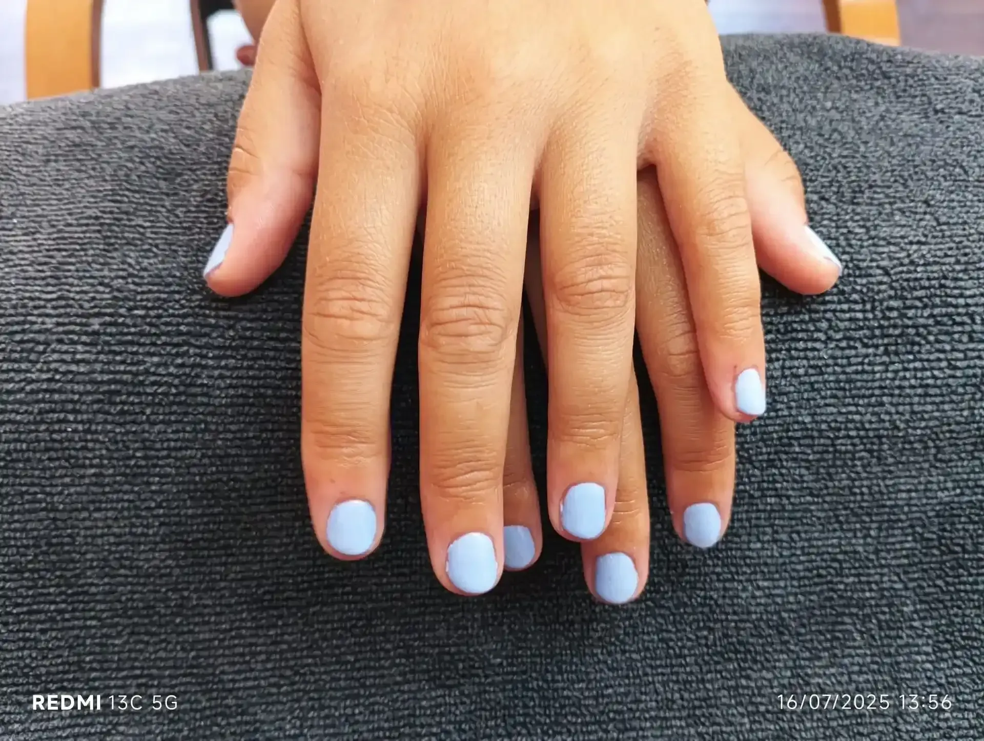 Manos con uñas cortas de color azul claro descansando sobre una toalla gris.