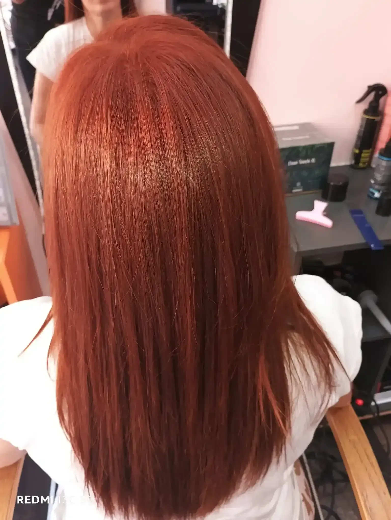 Mujer con cabello largo, liso y de un rojo intenso, sentada en una silla de peluquería. Su cabello luce recién peinado.