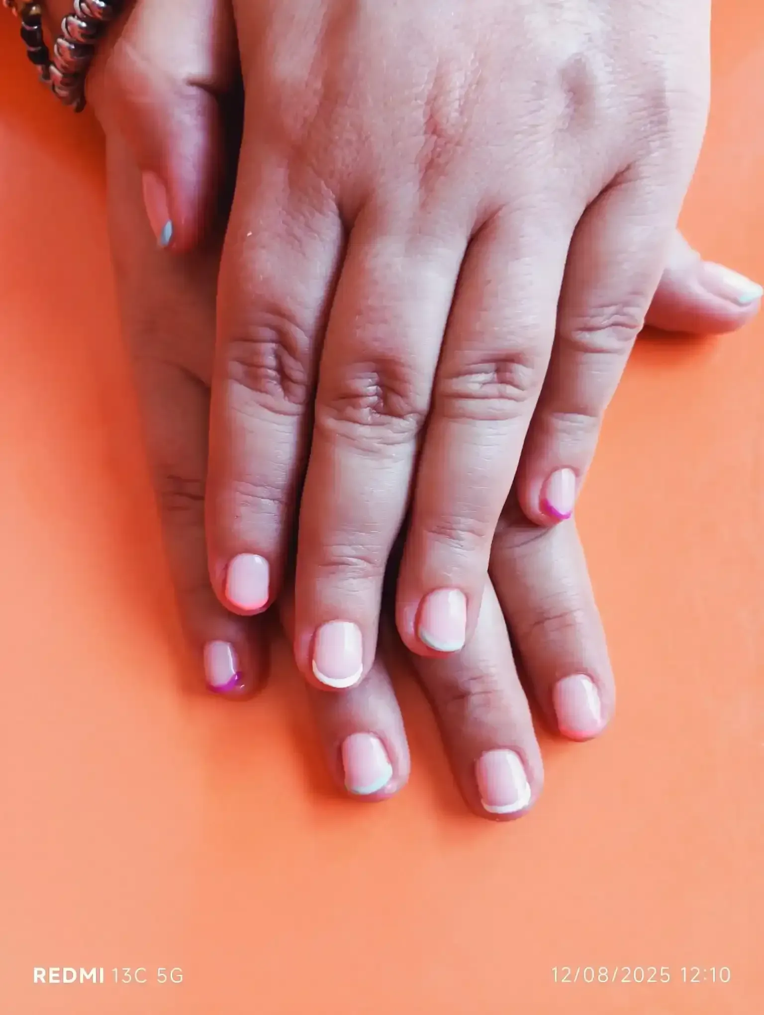 Manos con uñas de manicura francesa, pintadas de rosa y blanco, apoyadas sobre una superficie naranja.