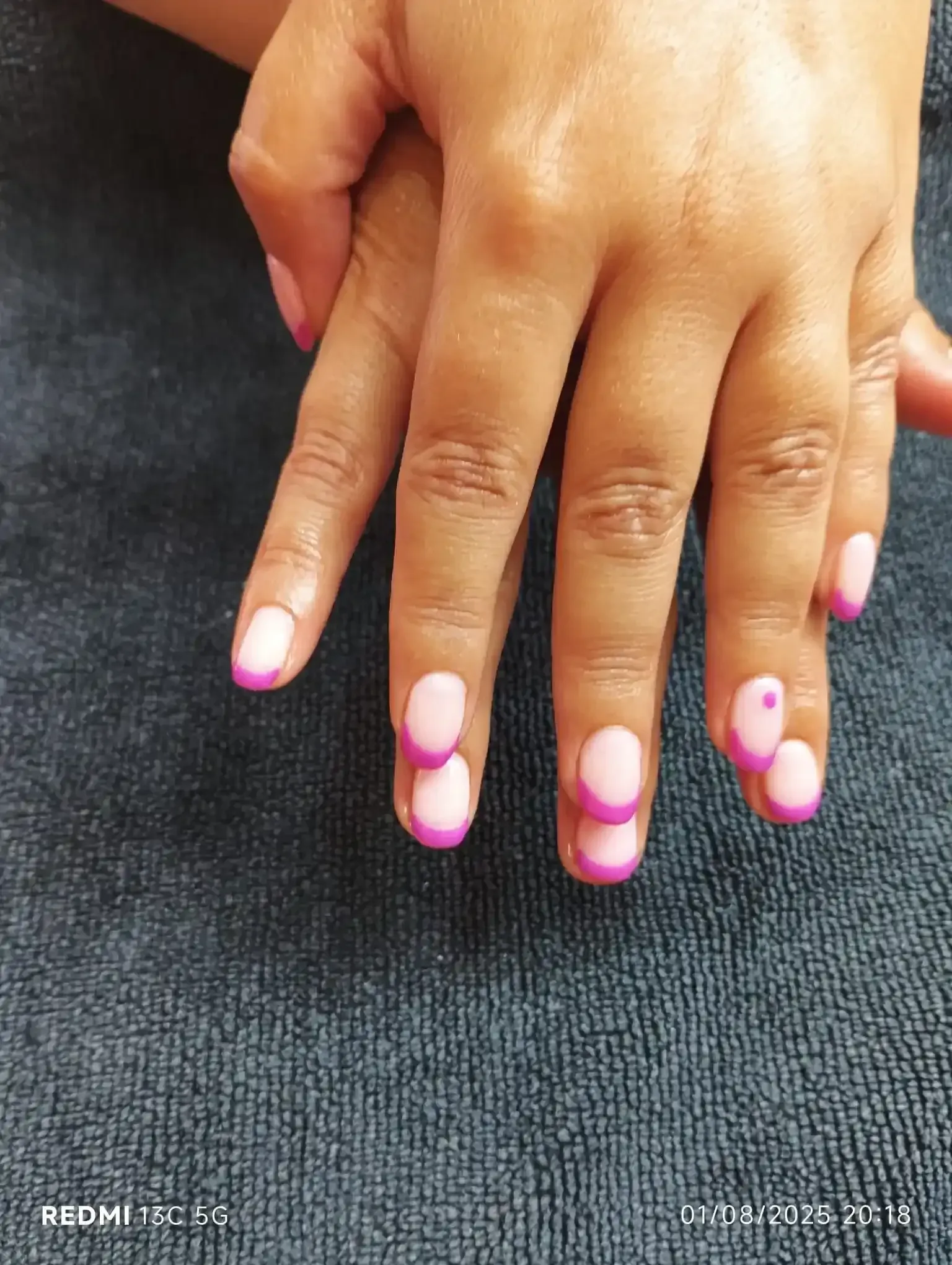 Uñas manicuradas con puntas rosas, descansando sobre una superficie azul texturizada.