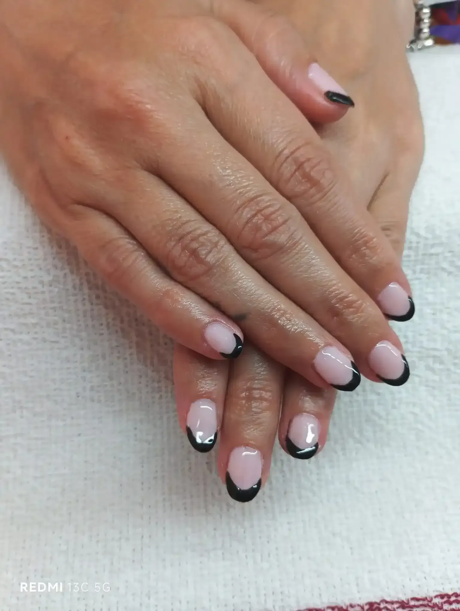 Manos con uñas rosa claro con puntas francesas negras.