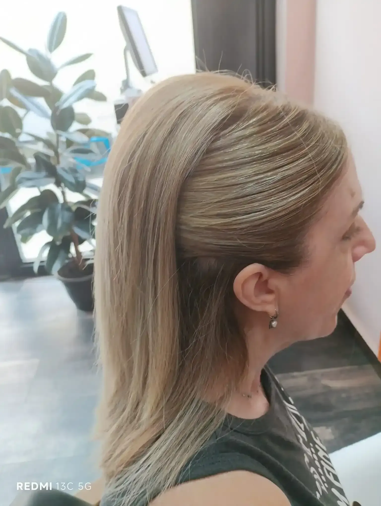 Mujer con cabello rubio claro recogido en un semirecogido, vestida con una camisa oscura, en interiores.