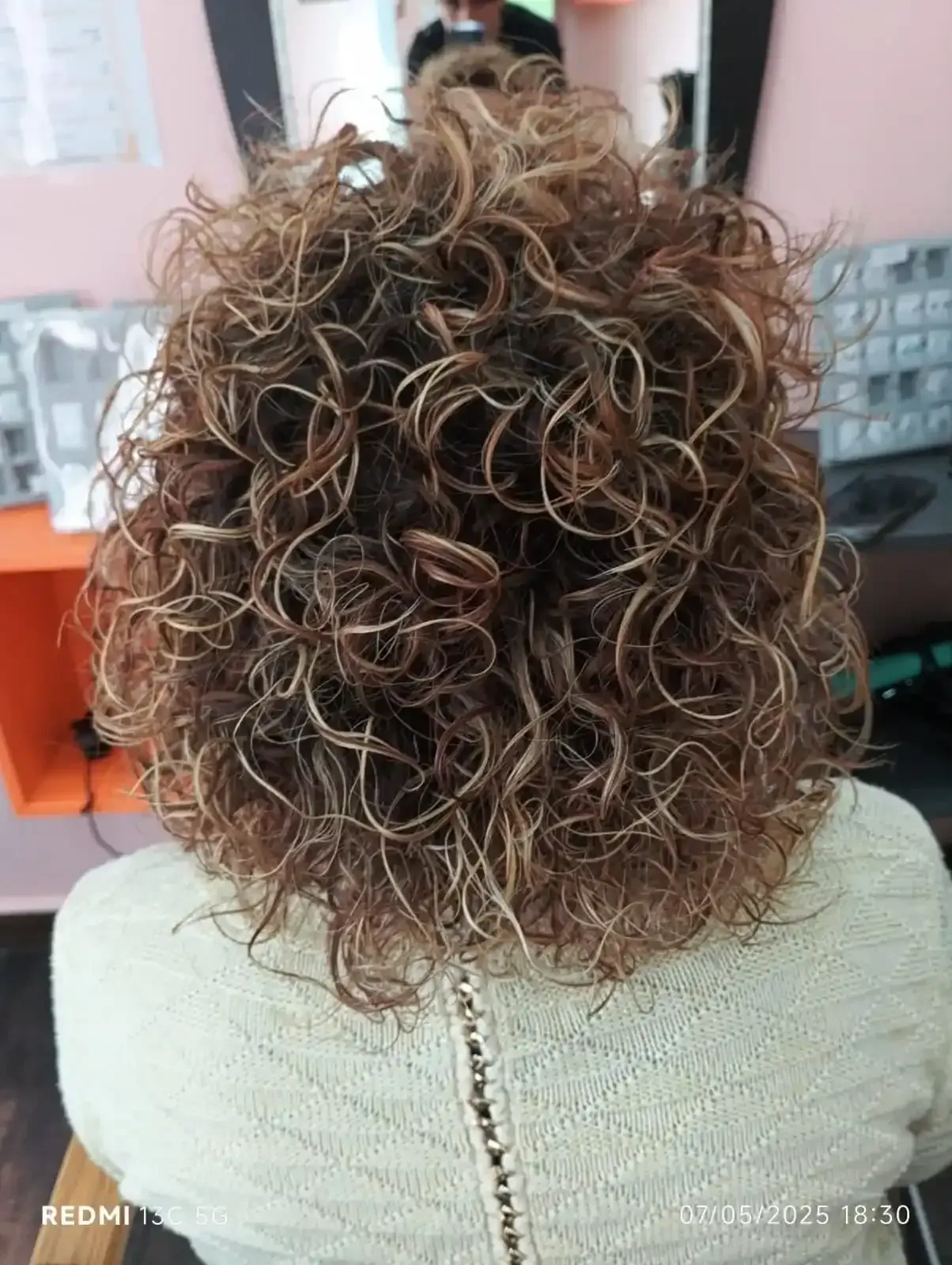 Persona con cabello rizado y con reflejos, vista de espaldas. Lleva un suéter color crema y está sentada.