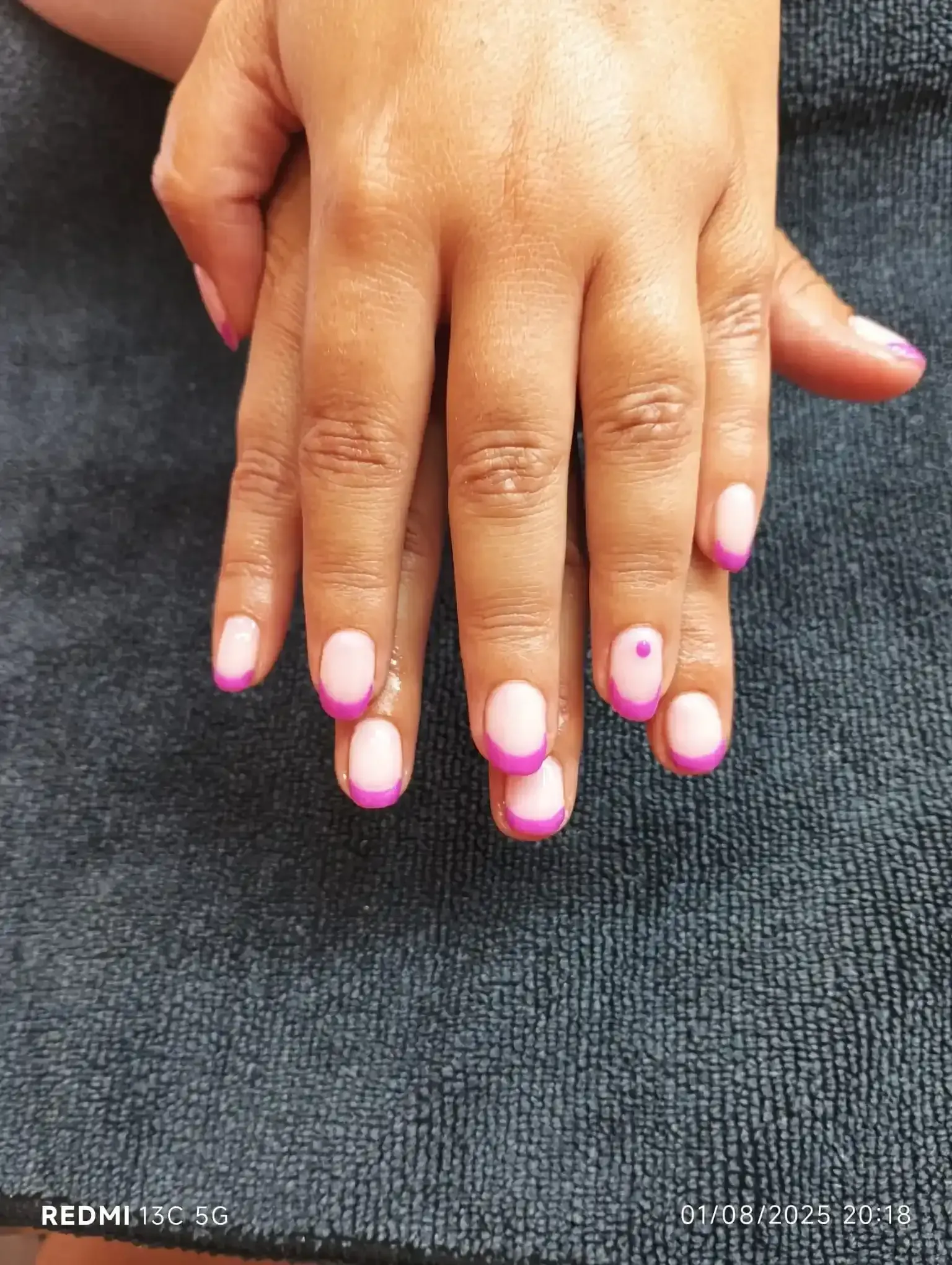 Manicura francesa rosa y morada en las manos de una persona. Una uña tiene un punto rosa.