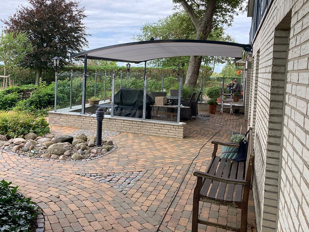 Ein Ziegelweg, der zu einer Terrasse mit einem Baldachin und einer Bank führt.