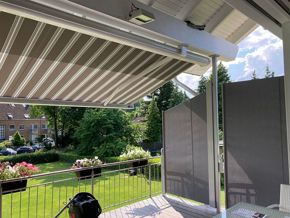 Eine Person sitzt auf einem Balkon mit einer gestreiften Markise darüber.