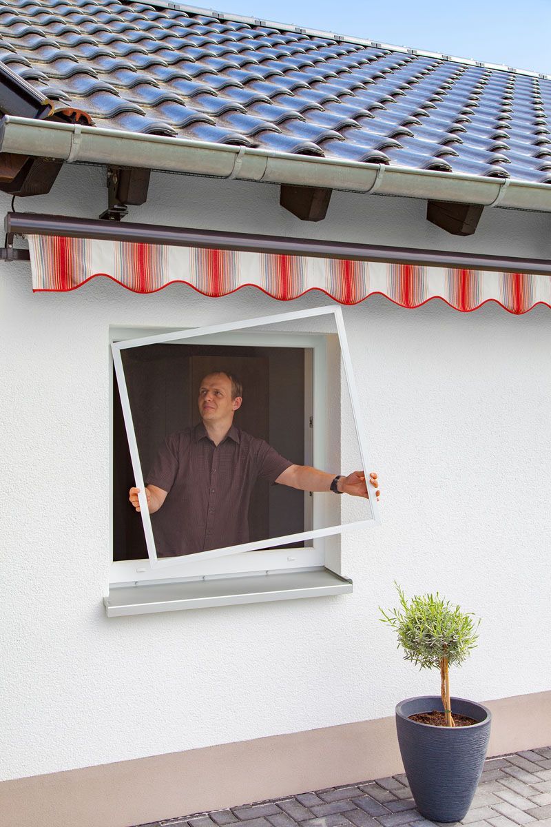 Ein Mann öffnet ein Fenster, an dem ein Moskitonetz befestigt ist.