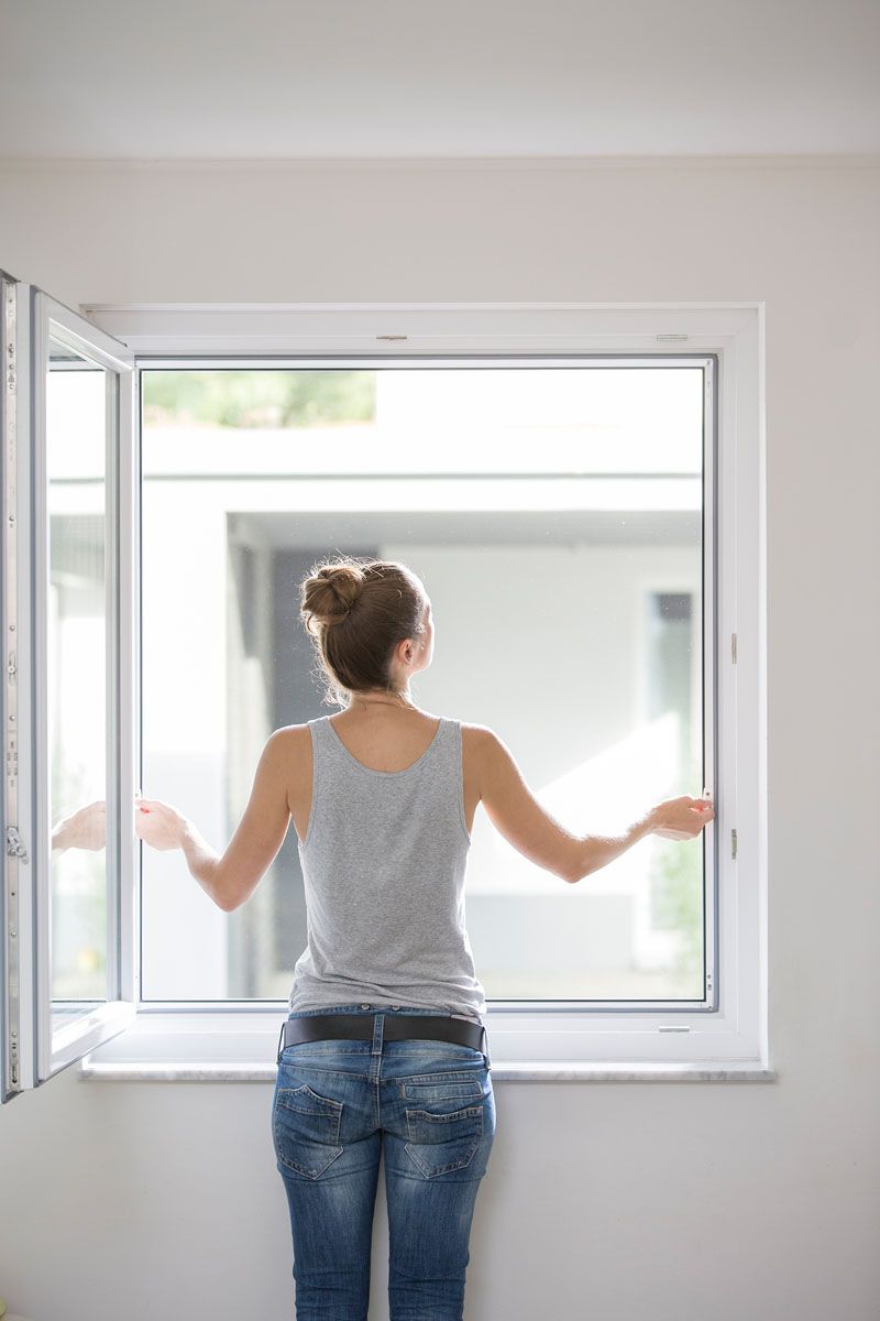 Eine Frau steht vor einem offenen Fenster.