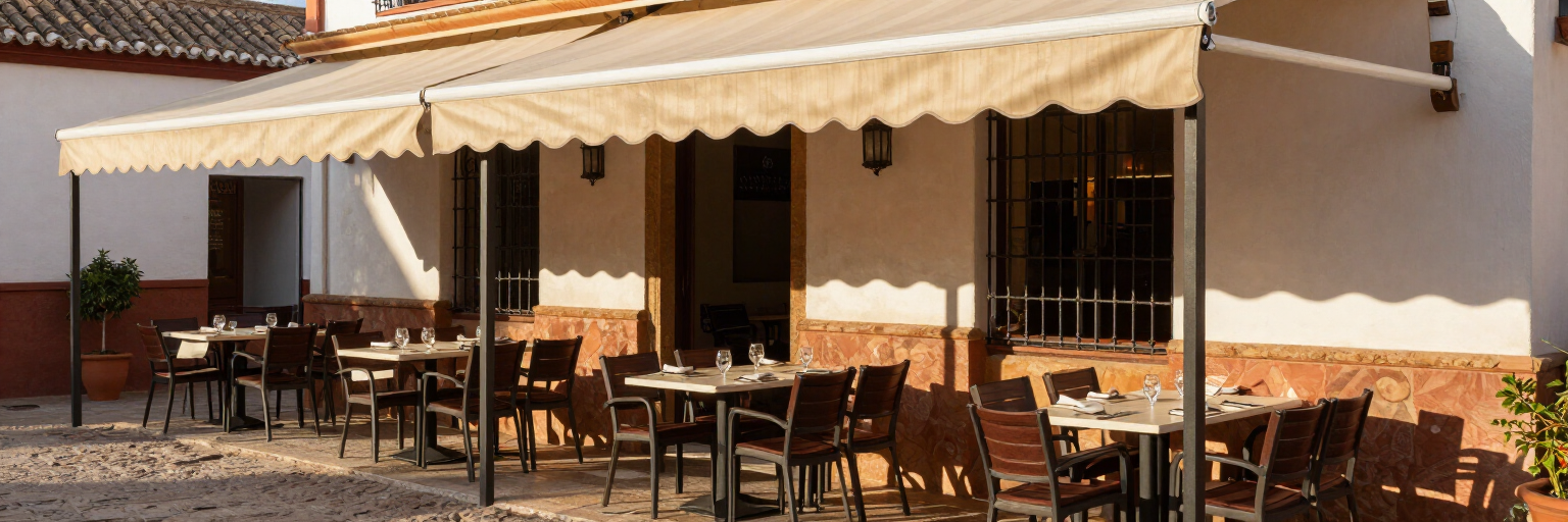 Terraza de café al aire libre con mesas y sillas vacías bajo toldos beige junto a un edificio
