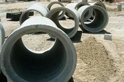 Um monte de tubos de concreto estão empilhados uns sobre os outros no chão.