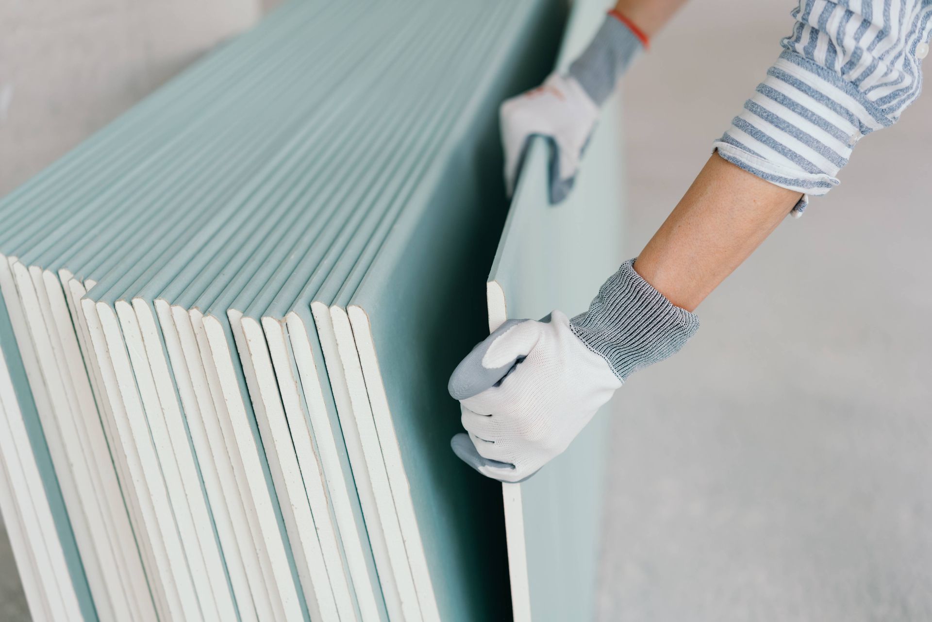 Uma pessoa está segurando uma pilha de folhas de drywall.