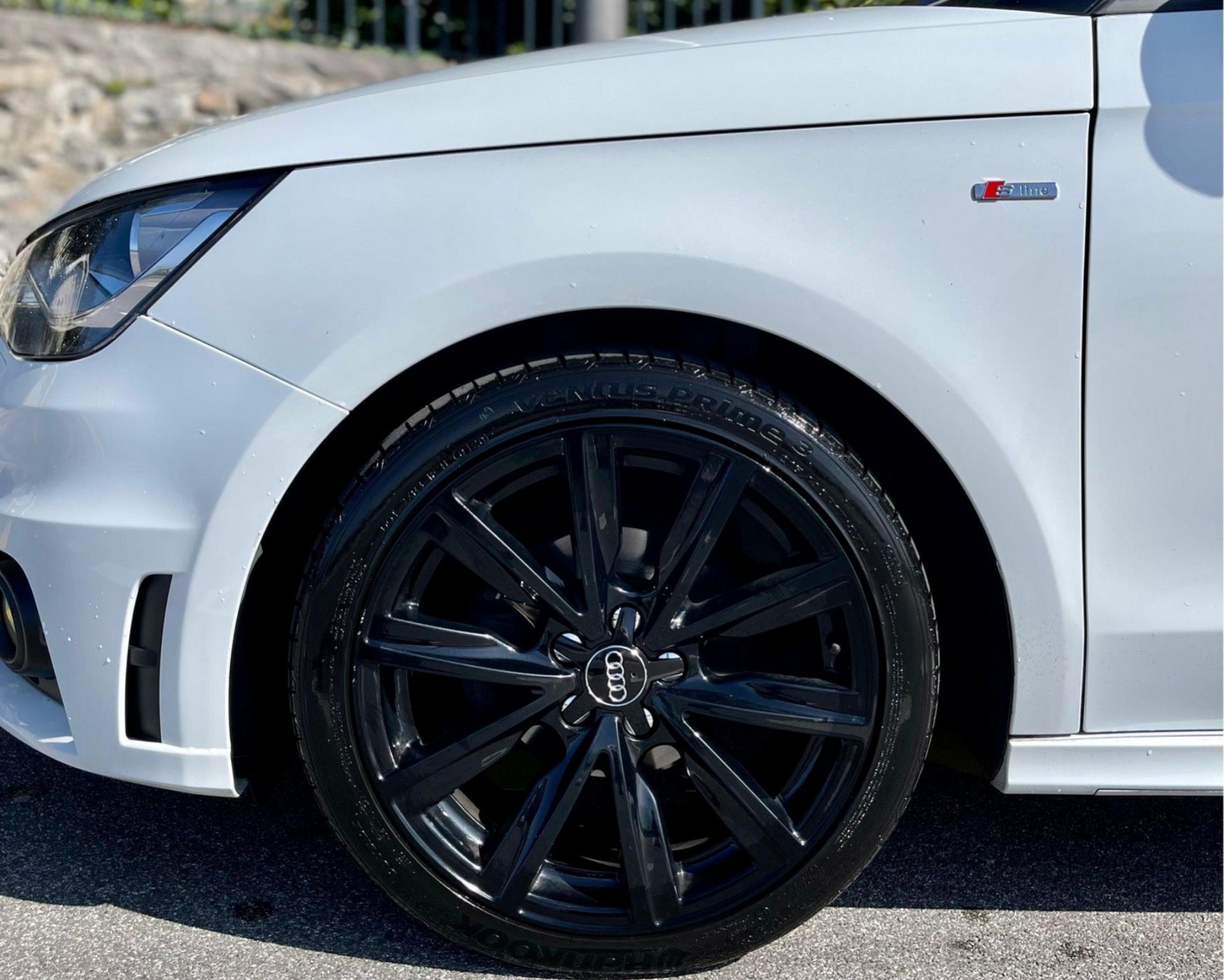 Audi A1 blanche avec jante noire, partiellement visible, à l'extérieur. Badge « S line ».