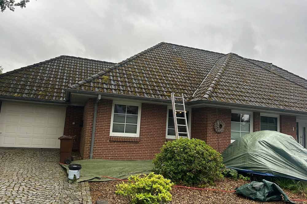 Ein Backsteinhaus mit einer Leiter auf dem Dach und einer grünen Plane davor.