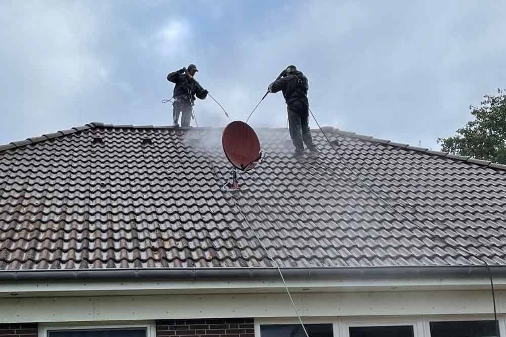 Ein Mann reinigt das Dach eines Hauses mit einem Hochdruckreiniger.