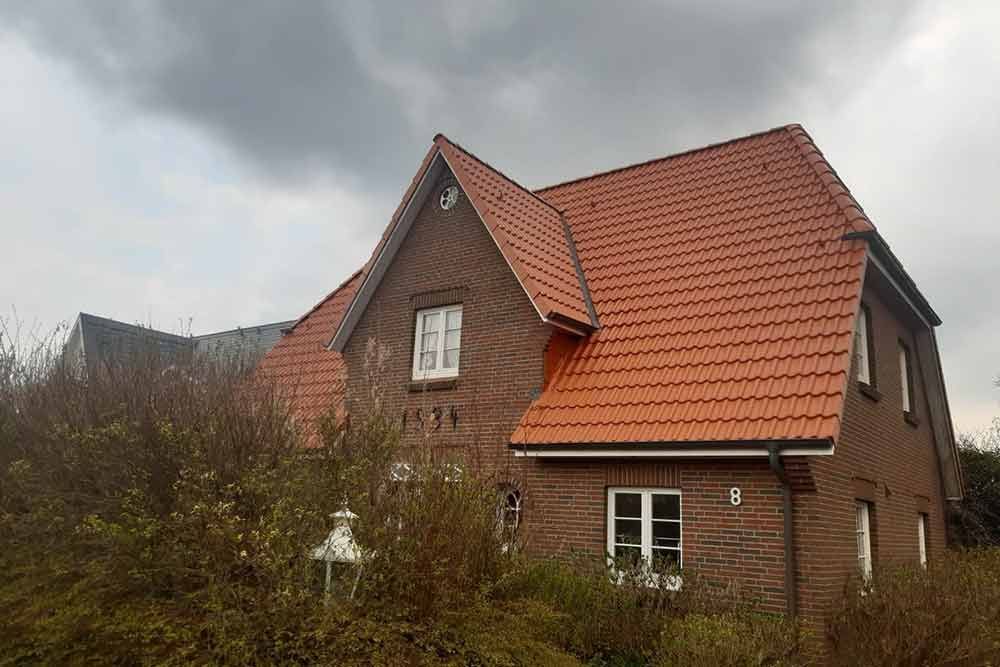 An einem bewölkten Tag ist ein Backsteinhaus mit einem roten Ziegeldach von Büschen umgeben.