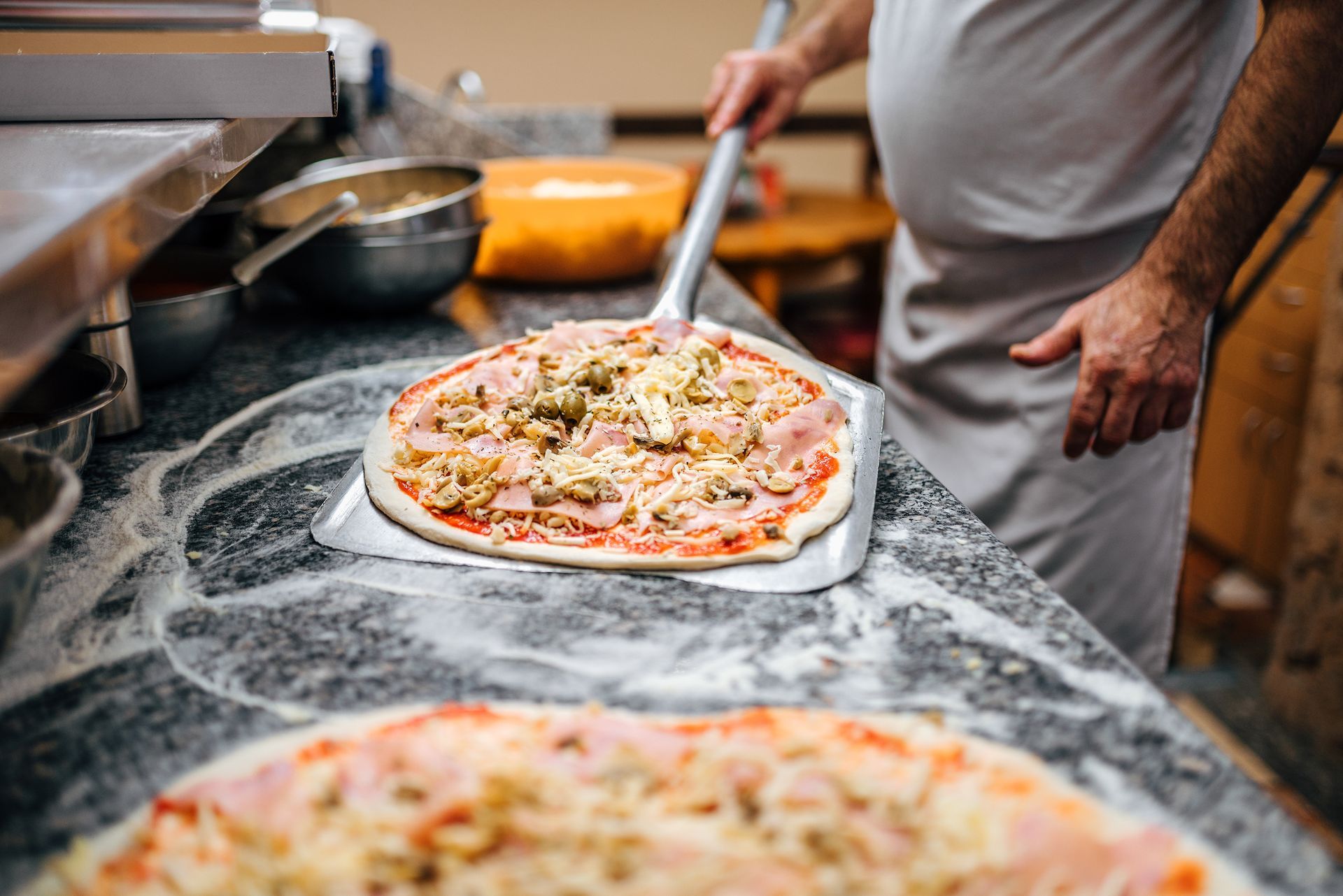 Un pizzaïolo prépare une pizza à l'aide d'une pelle.