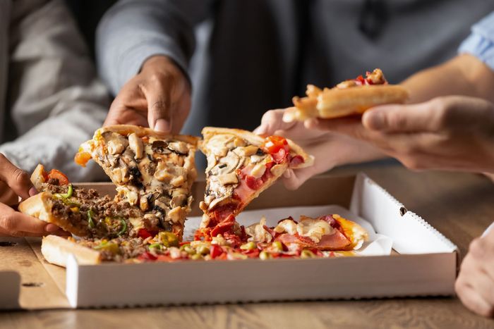 Des mains se tendent vers une boîte ouverte pour attraper des parts de pizza, partageant un repas.
