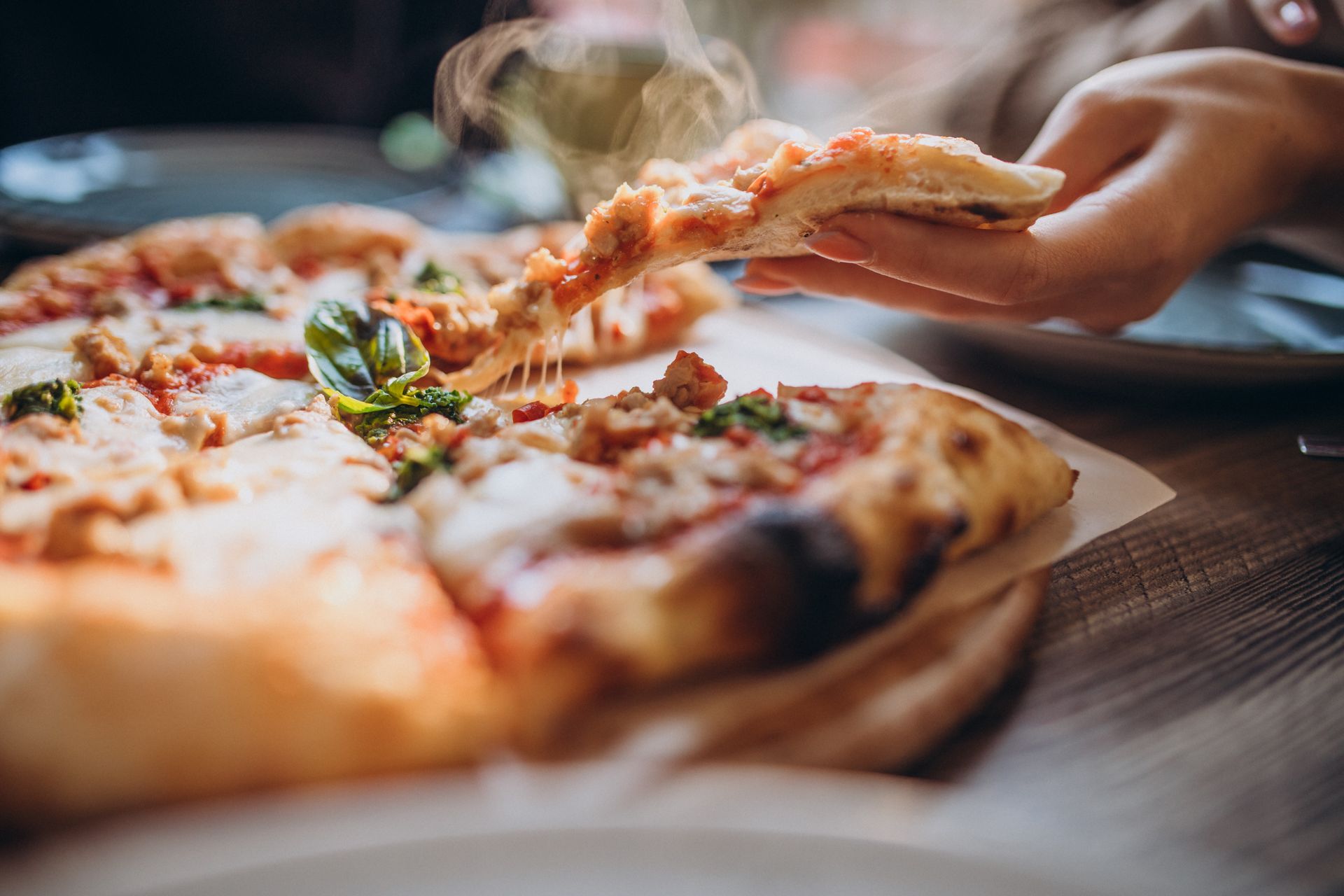 Une part de pizza est prélevée d'une pizza entière posée sur une surface en bois, de la vapeur s'en échappant.