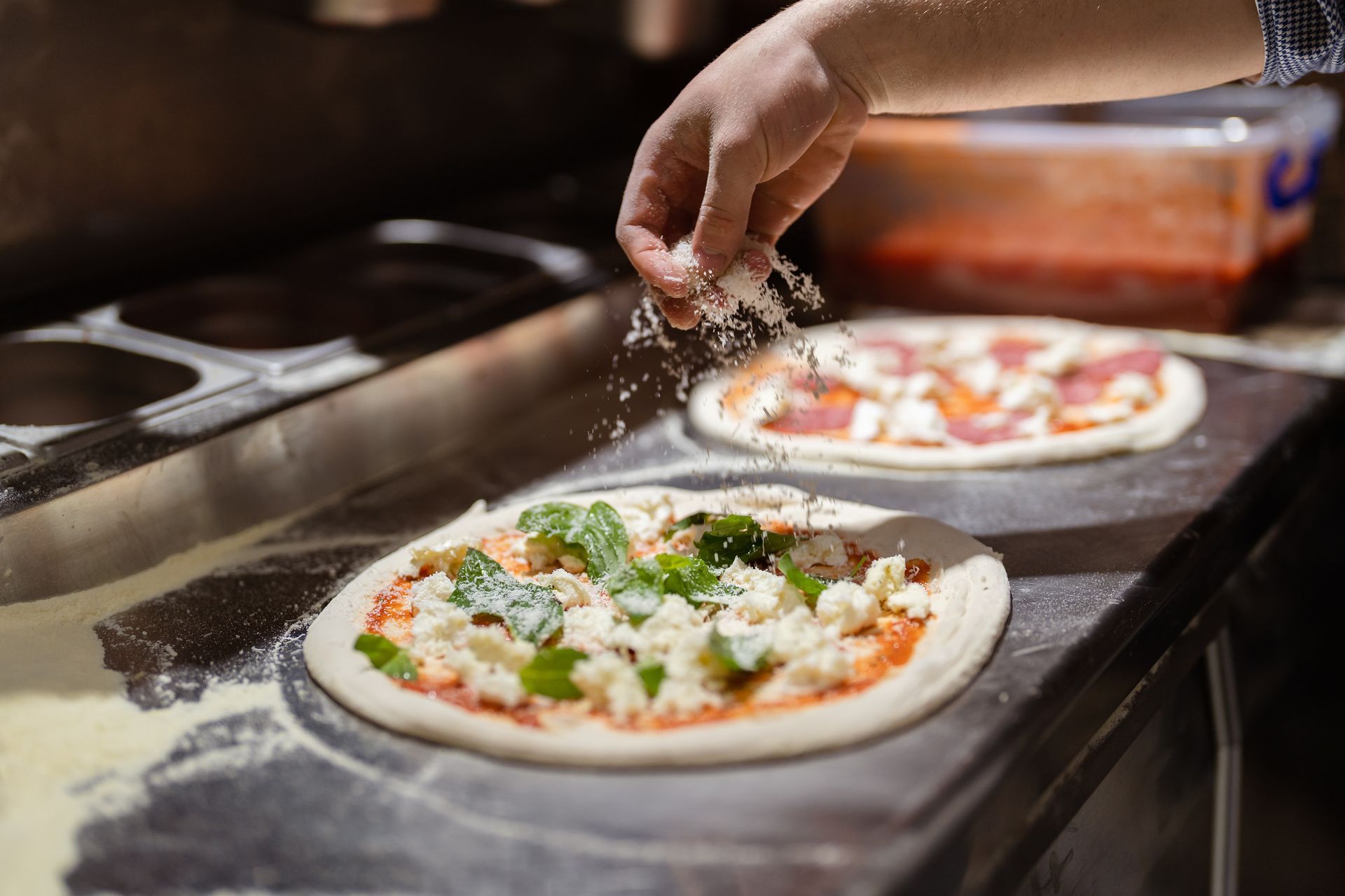 Gros plan sur deux pizzas saupoudrées de fromage. L'une est garnie de basilic, l'autre de sauce tomate et de fromage.