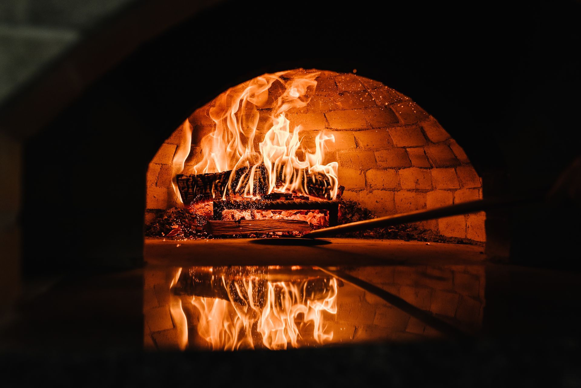 Four à bois en briques, avec des flammes et des braises incandescentes se reflétant sur la surface sombre en dessous.