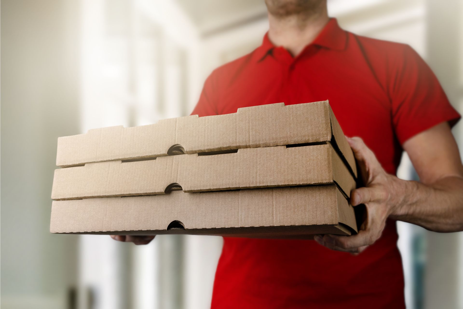 Une personne en chemise rouge tenant trois boîtes à pizza empilées à l'intérieur.