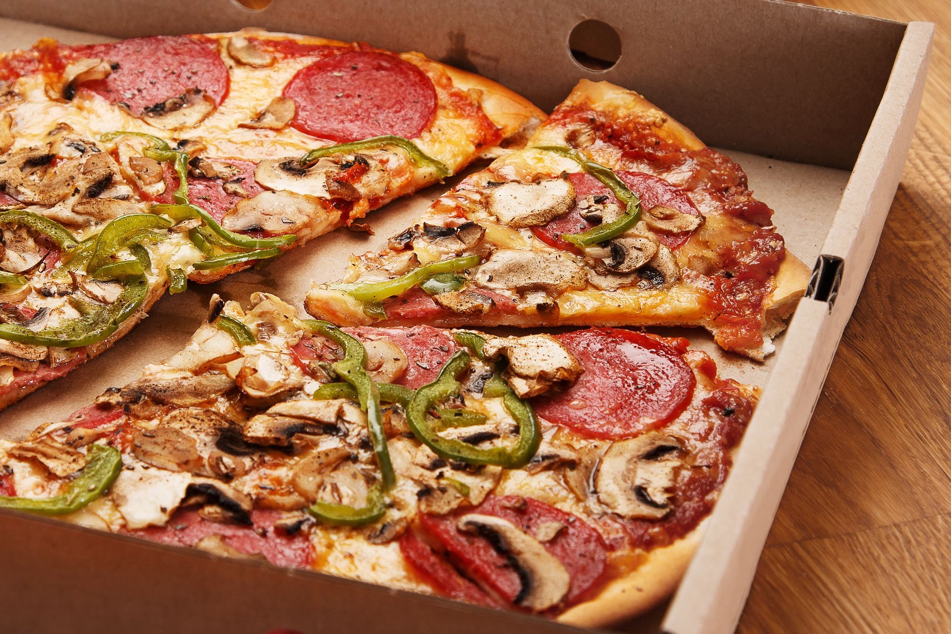 Pizza dans une boîte en carton, garnie de pepperoni, de poivrons verts et de champignons.