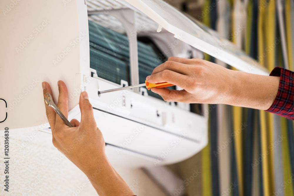Une personne répare un climatiseur avec un tournevis.