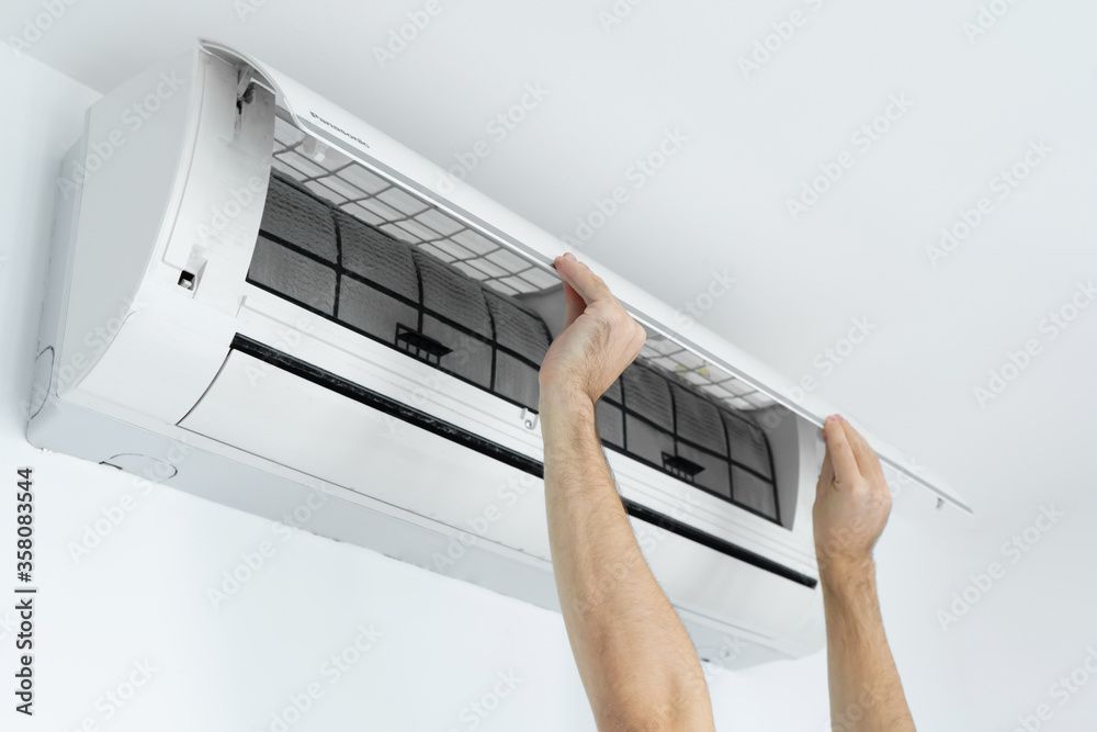 Une personne répare un climatiseur avec un tournevis.