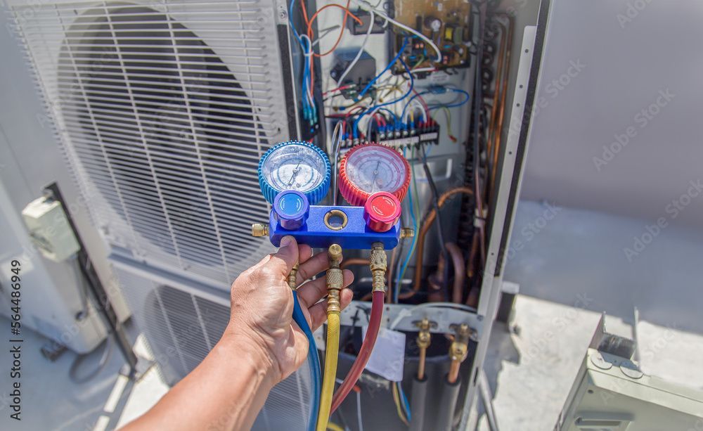 Une personne travaille sur un climatiseur avec une jauge.