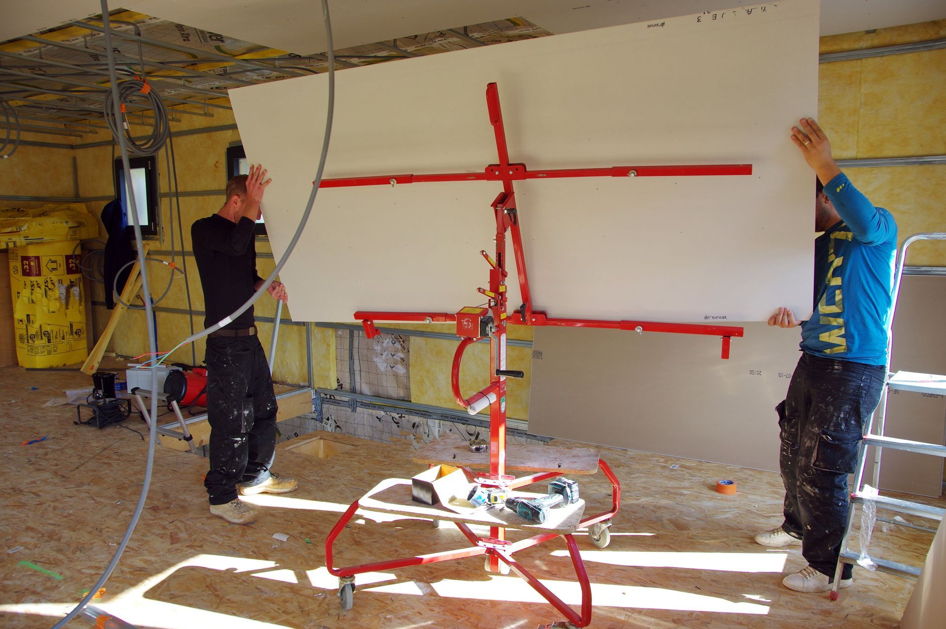 Deux plaquistes installant une grande plaque de plâtre.
