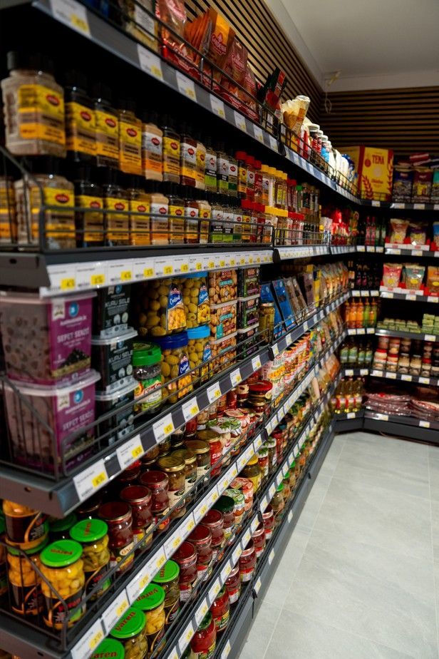Une allée de supermarché bordée de bocaux, de sauces et d'aliments emballés sur de hautes étagères.