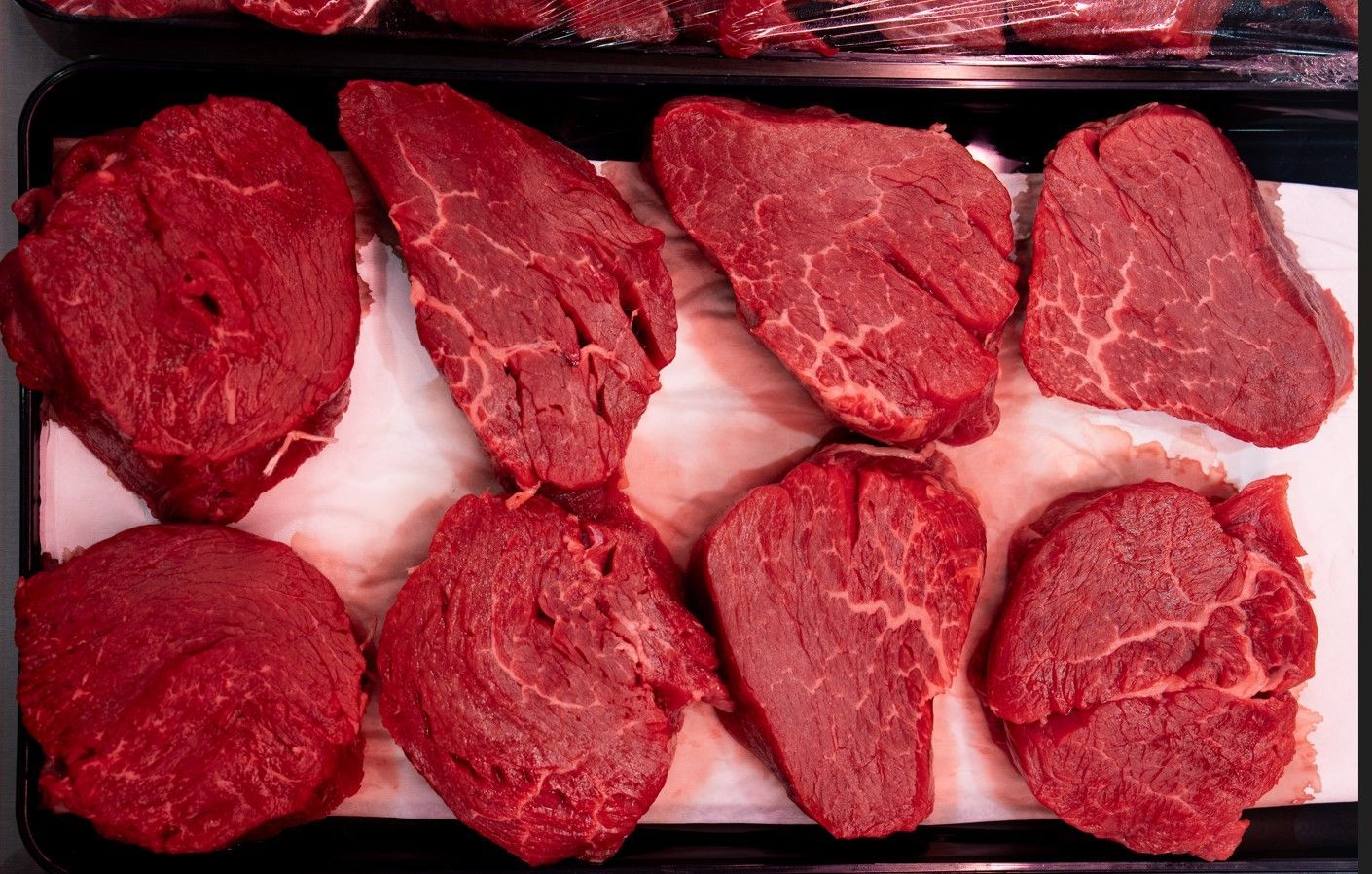 Des steaks de bœuf crus disposés sur un plateau, rouges et non cuits, avec du papier blanc entre les morceaux.