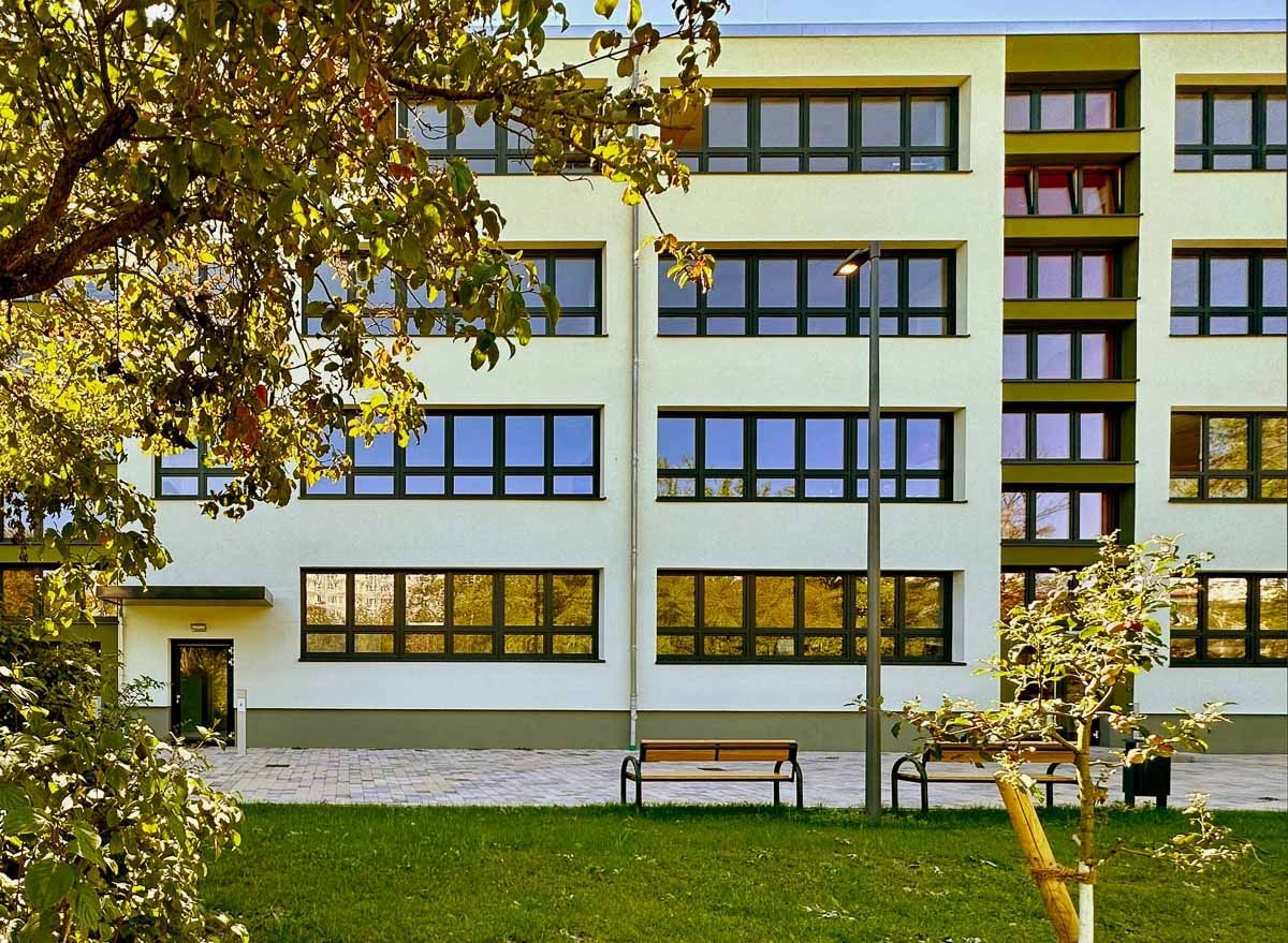 ein großes weißes Gebäude mit vielen Fenstern und einem Park davor - Referenzen von BAUSON GmbH aus Gräfenhainichen