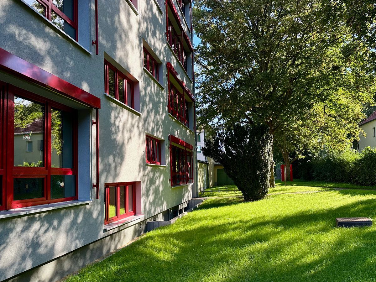 ein graues Gebäude mit roten Fenstern und einem grünen Rasen davor - Referenzen von BAUSON GmbH aus Gräfenhainichen